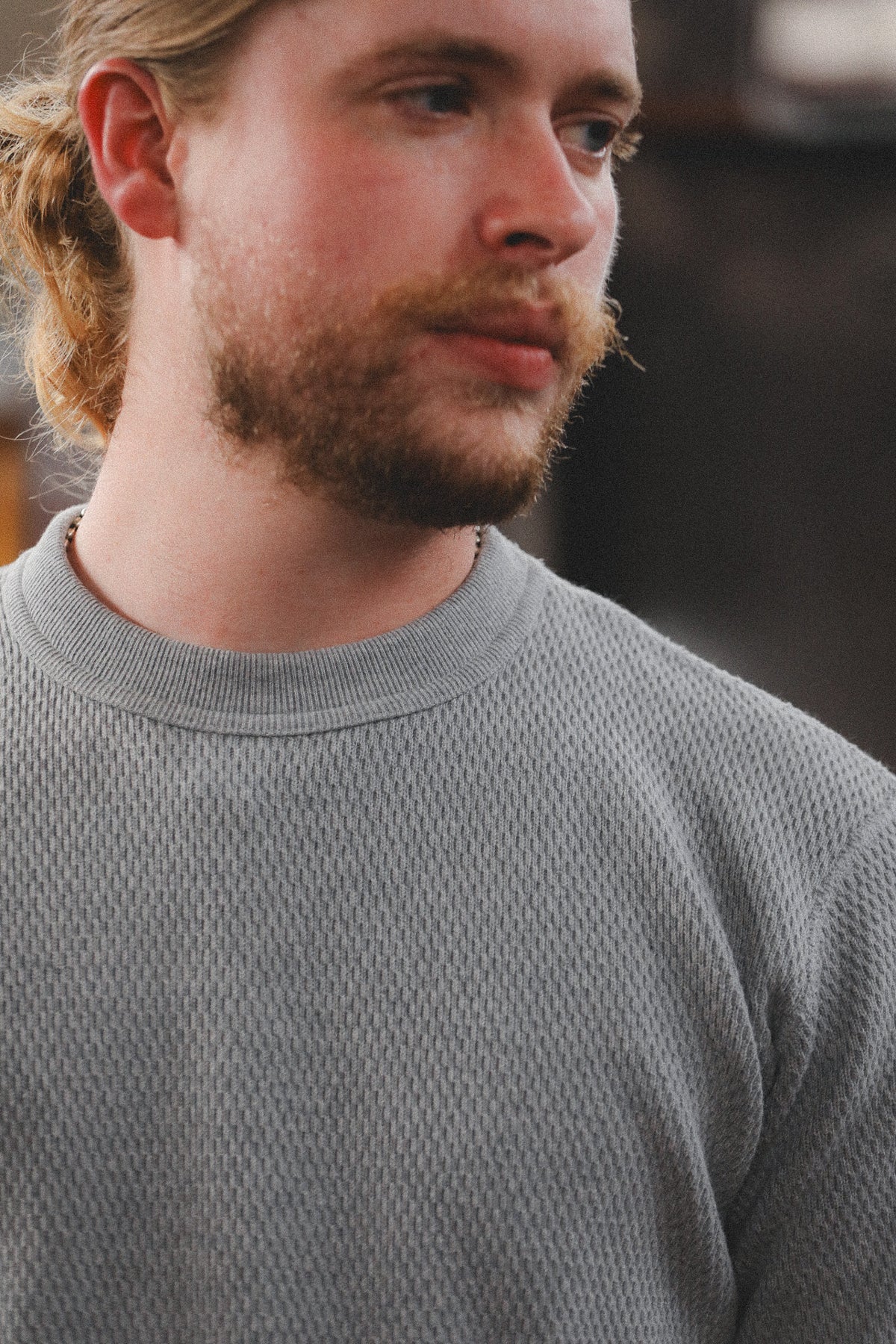 A close-up shot of a man wearing a textured gray crewneck sweater, showing his face in profile and the knit fabric detail.