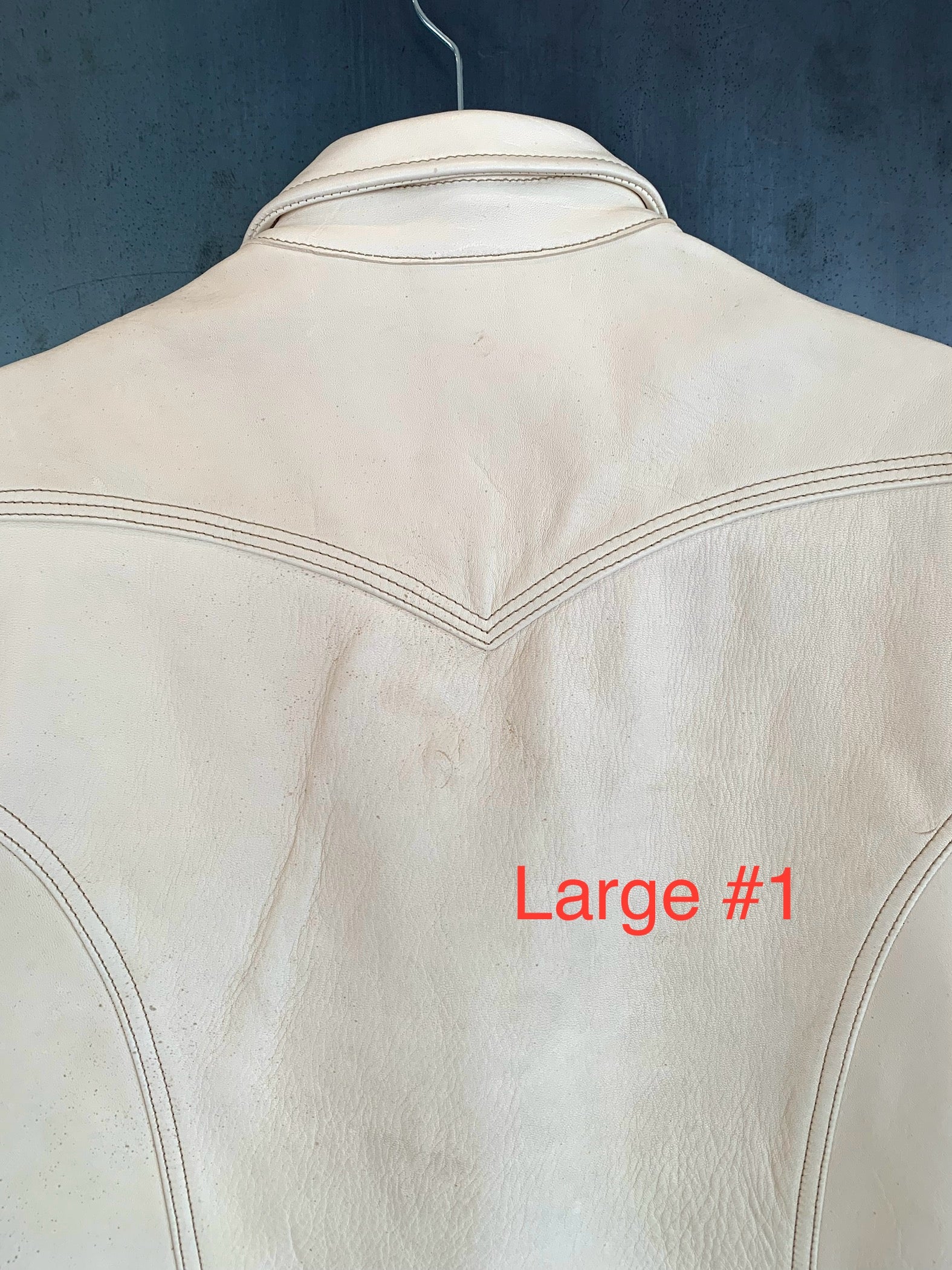 Close-up of the back of a cream leather jacket with stitched detailing and collar, hanging on a dark hanger