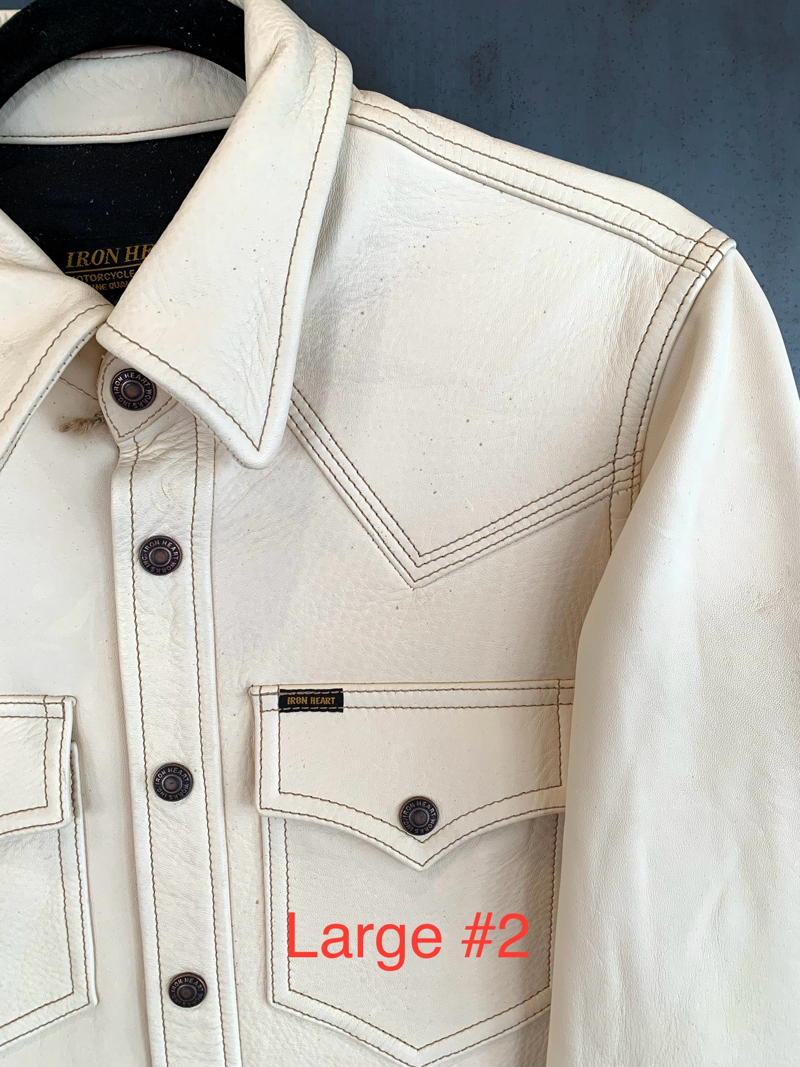 Close-up of cream leather jacket with Iron Heart logo label and snap buttons on front pocket