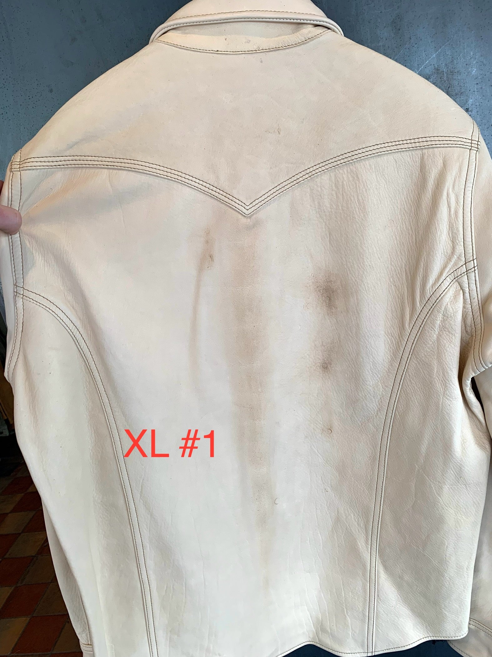 Back view of off-white vintage leather jacket with worn marks and stitching details held by hand