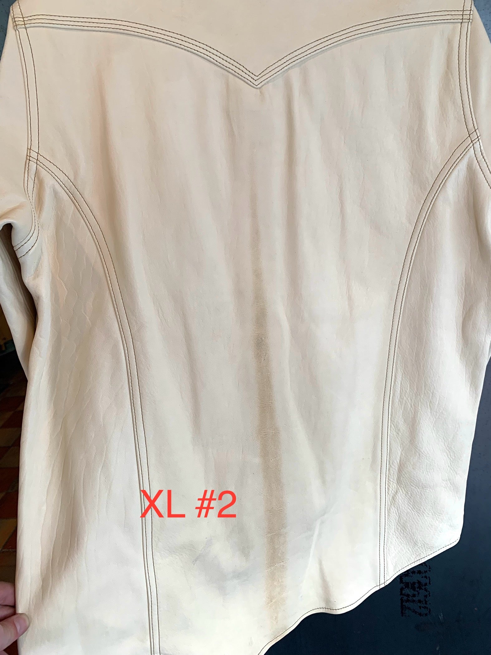 Back of an off-white leather jacket with detailed seam stitching and a faint mark, held by a person