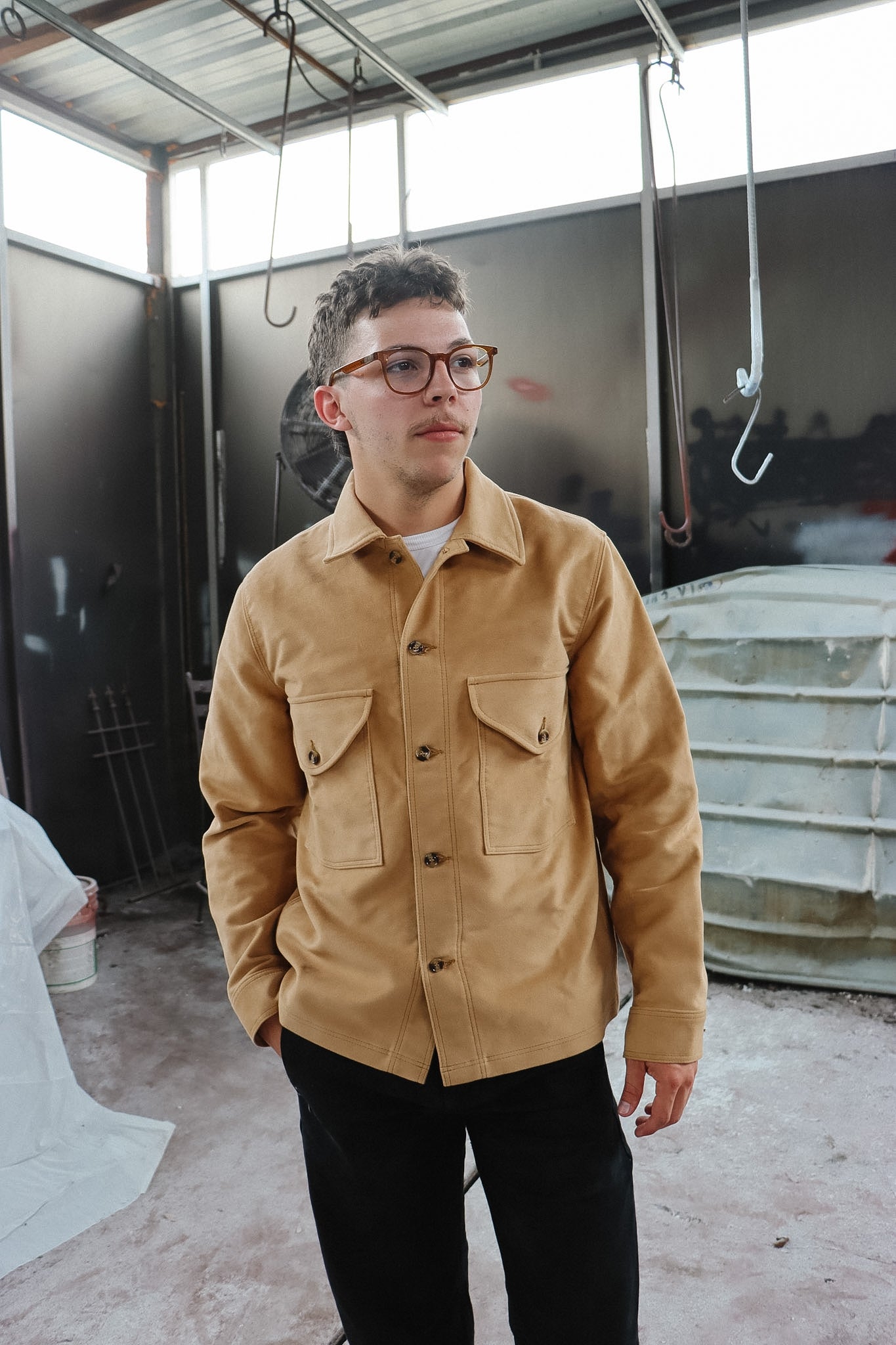 Person wearing a beige jacket in an indoor setting with a dark wall and light floor.