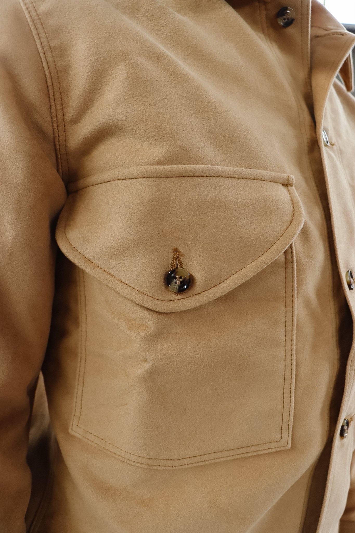 Close-up of a beige jacket with a pocket and buttons.