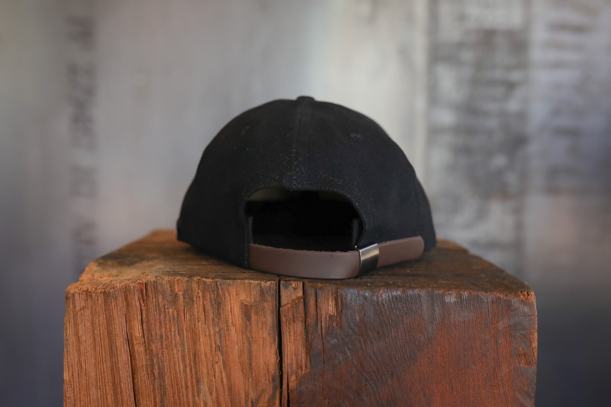 Black cap with brown strap on a wooden block against a blurred background