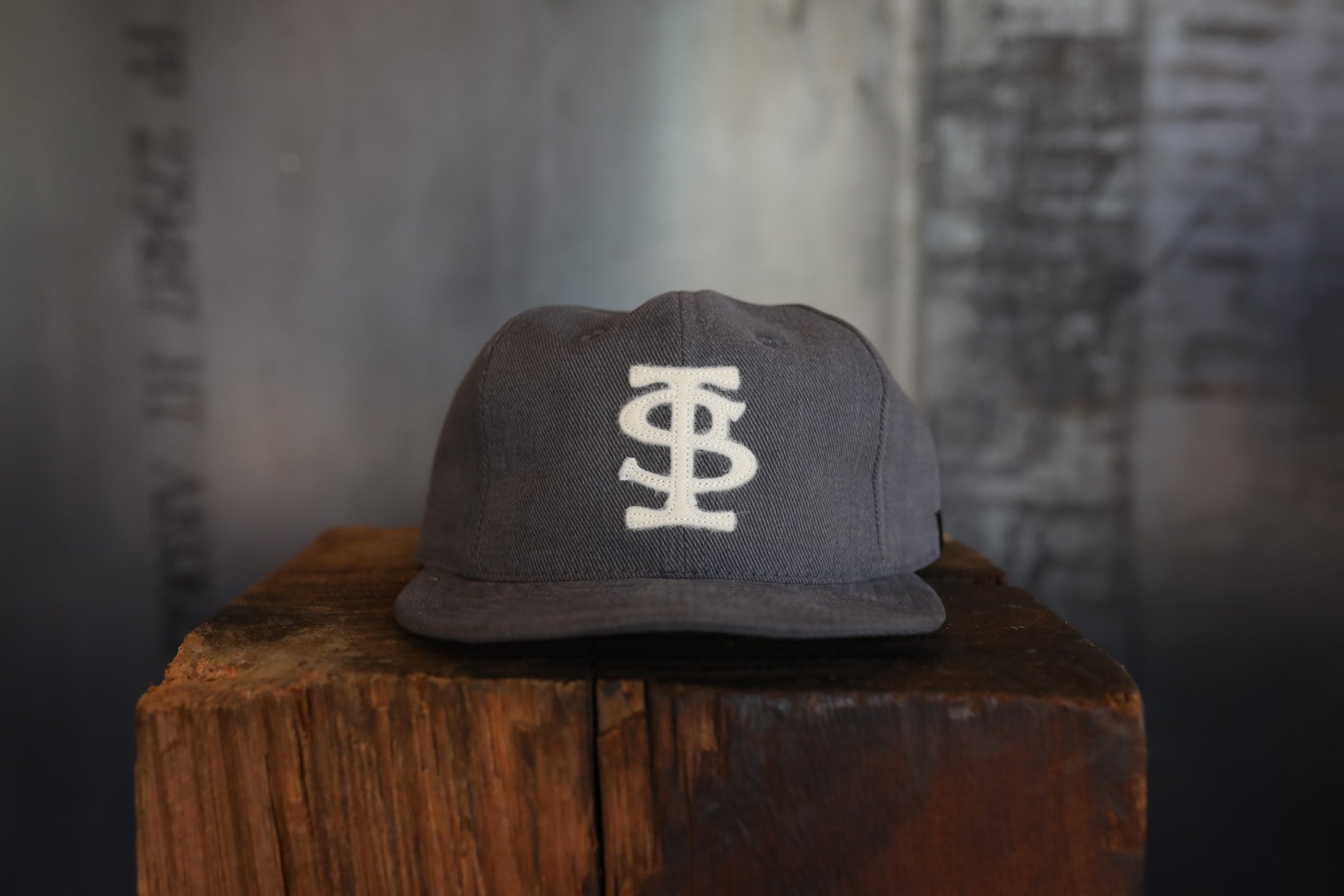 Gray cap with a logo on a wooden block against a textured wall.