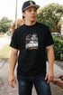 Young man wearing black Truckin Loopwheel tee with vintage truck and skeleton design outdoors