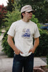 Man wearing cream Truckin Loopwheel tee with vintage truck and skeleton graphic, outdoors with greenery