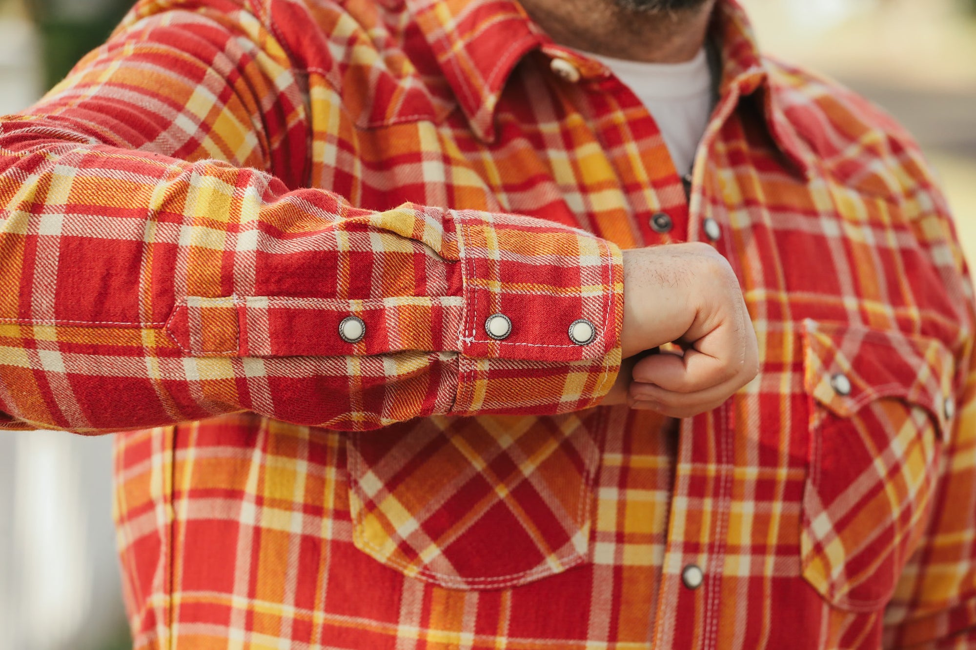 Close-up of a person wearing a red and yellow plaid shirt with rolled-up sleeves.