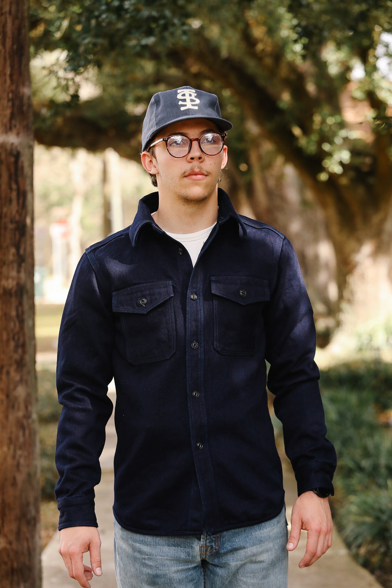 Person wearing a navy jacket and cap outdoors with trees in the background