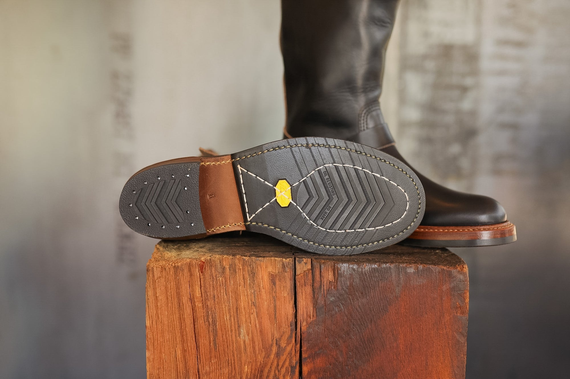 Close-up of a brown leather boot with a visible sole on a wooden block against a blurred background