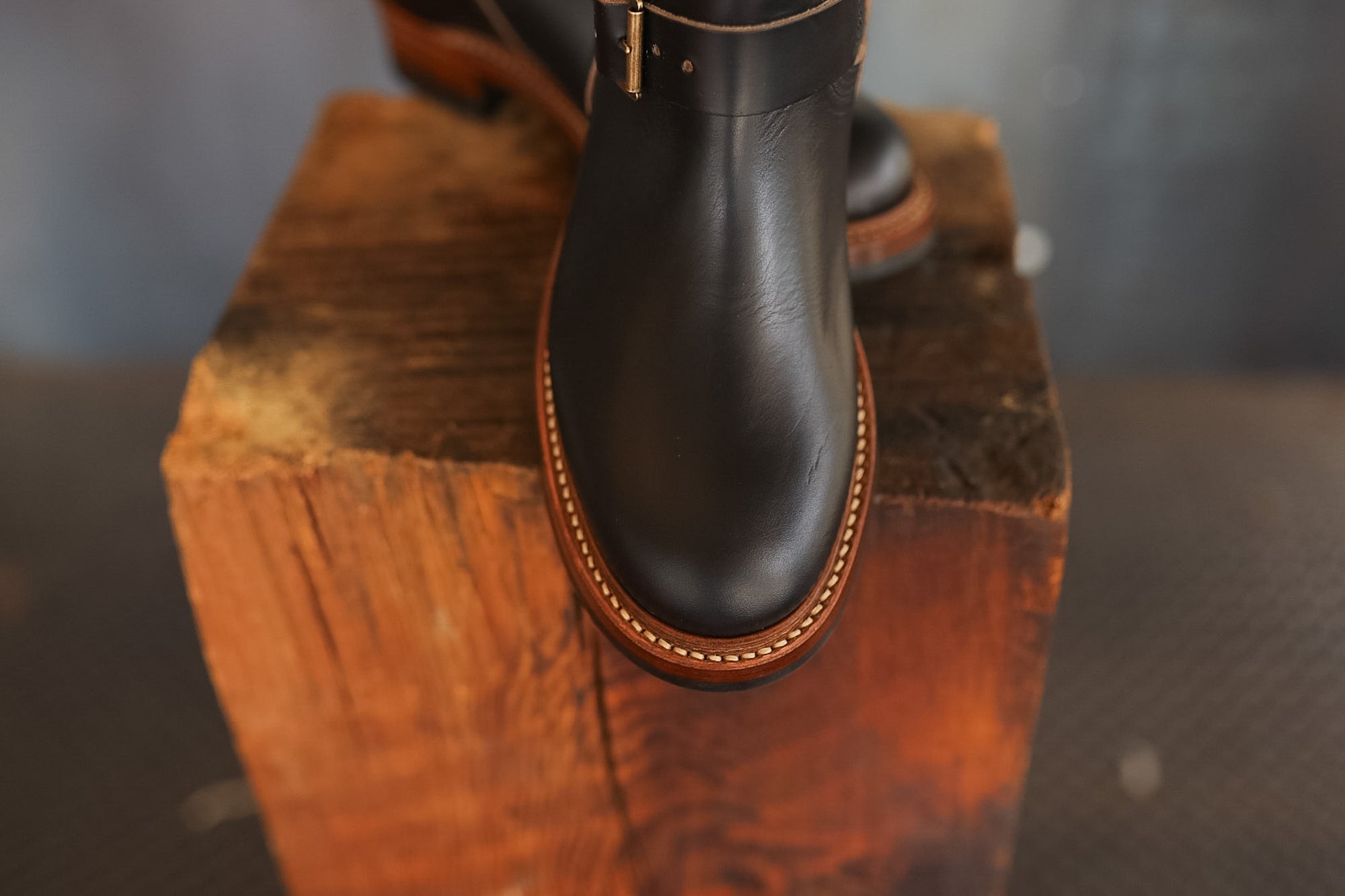 Black leather boot with brown trim on a wooden block against a blurred background