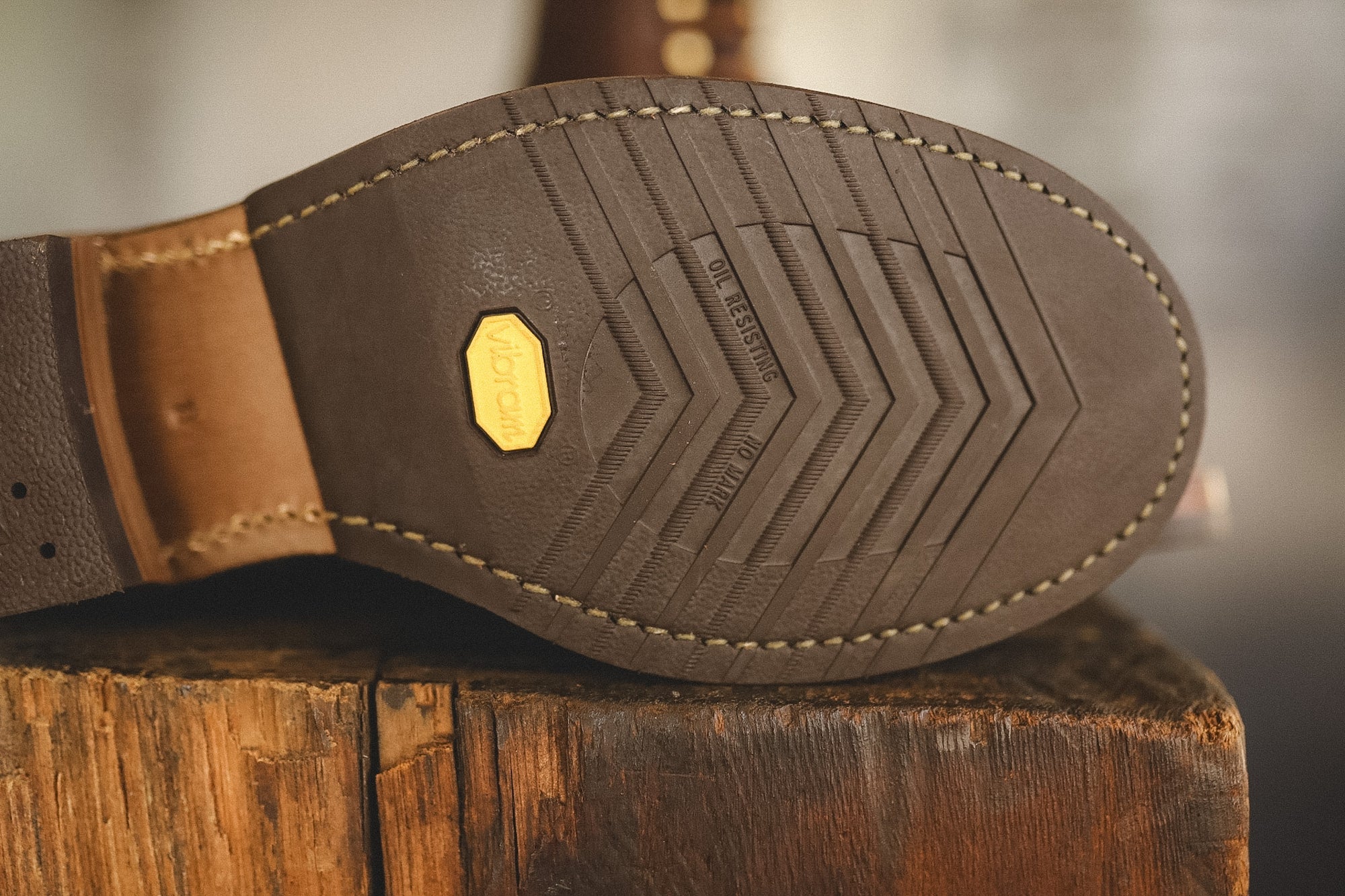 Close-up of the outsole of a brown leather shoe resting on a rustic wooden block, showing a Vibram logo on the tread.