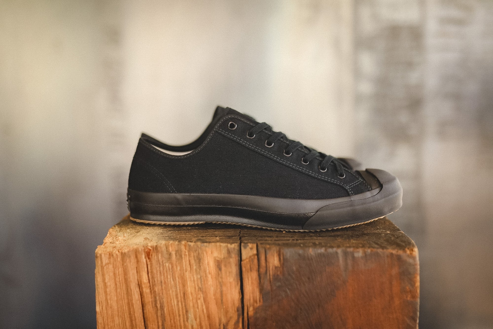 Up close image of a black sneaker on a wood block with a grey background 