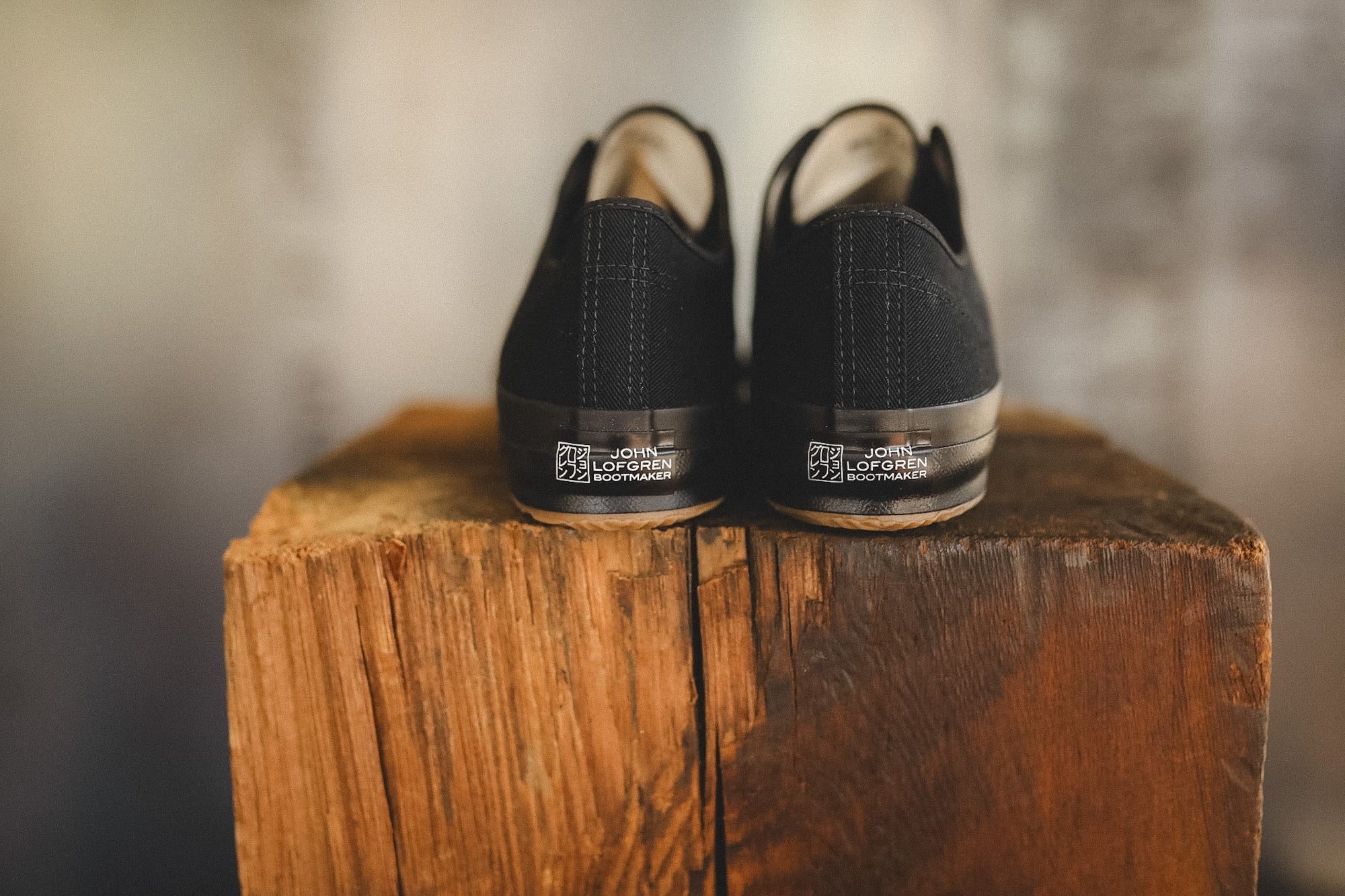 Up close image of a black sneaker on a wood block with a grey background 
