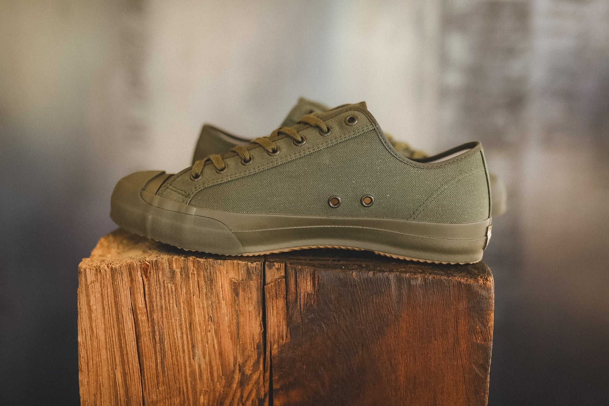 Up close image of a olive green sneaker on a wood block with a grey background 