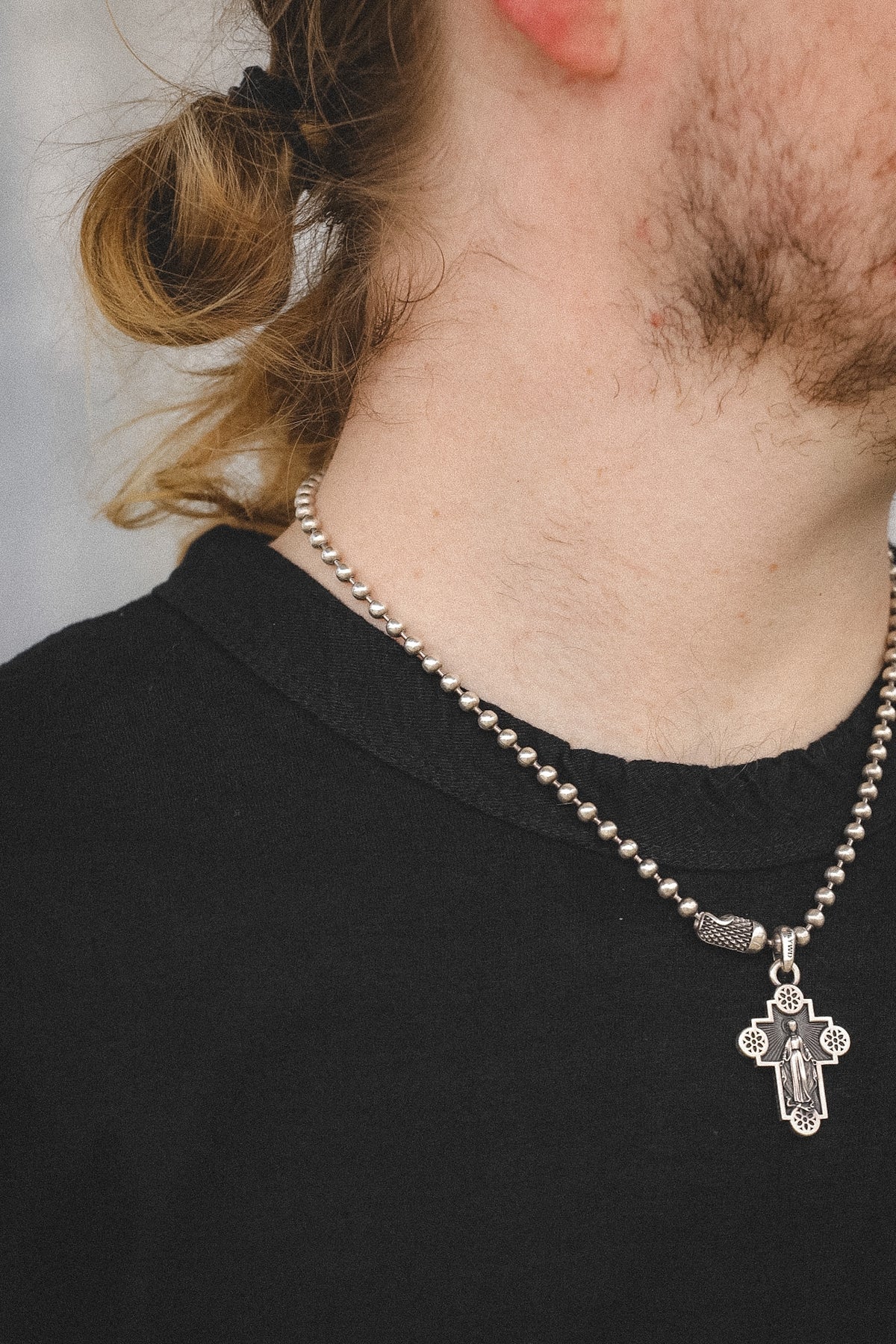 A close-up of a person's neck and lower face wearing a silver beaded chain necklace with a detailed crucifix pendant.