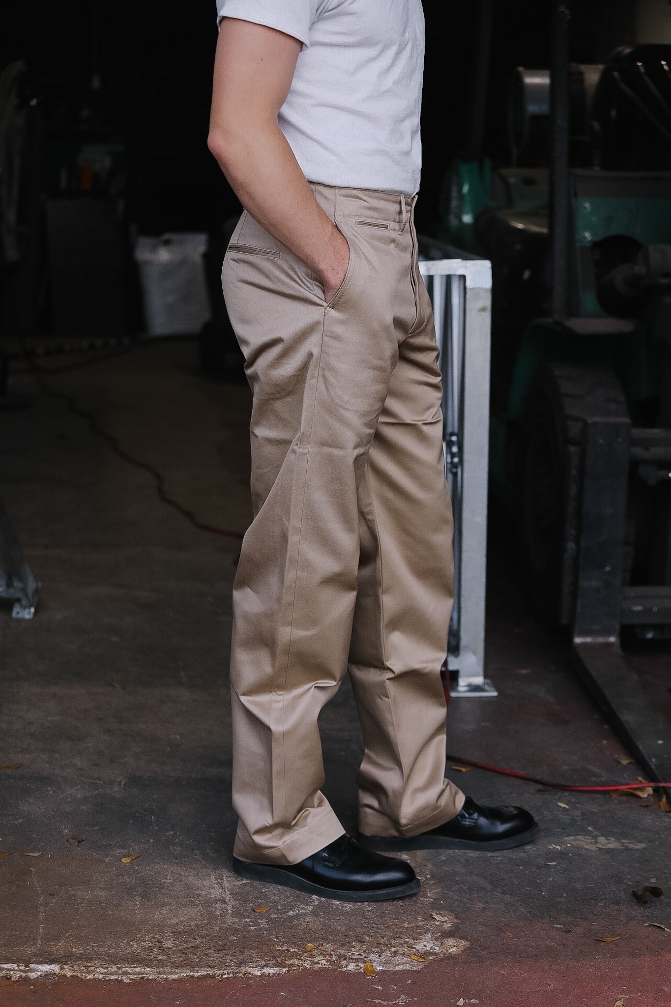 Person wearing beige pants and black shoes standing in a workshop.