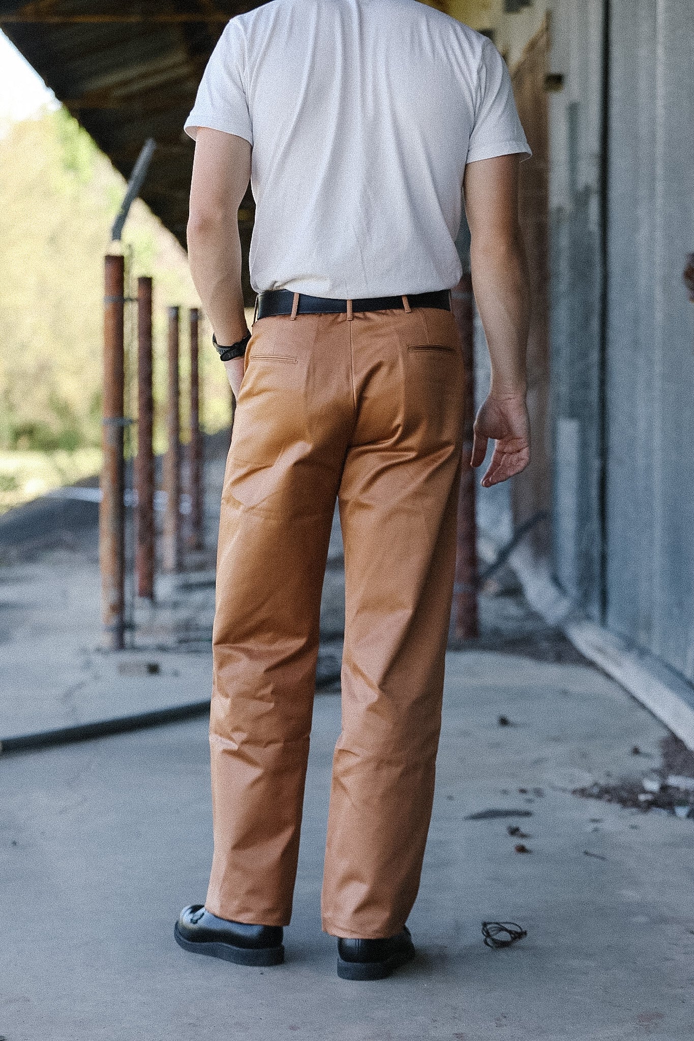 Person wearing brown pants and a white shirt standing on a concrete surface.