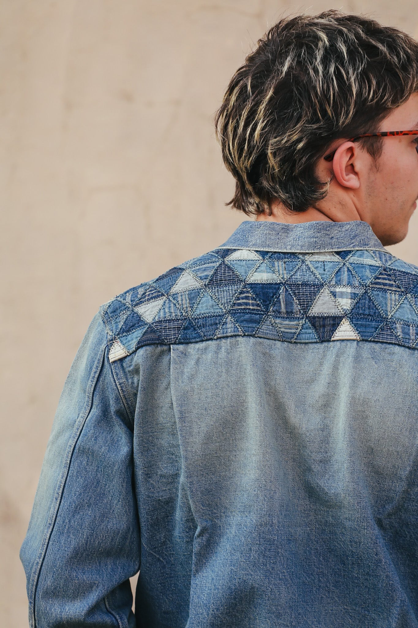 Person wearing a blue denim shirt with geometric pattern on a beige background