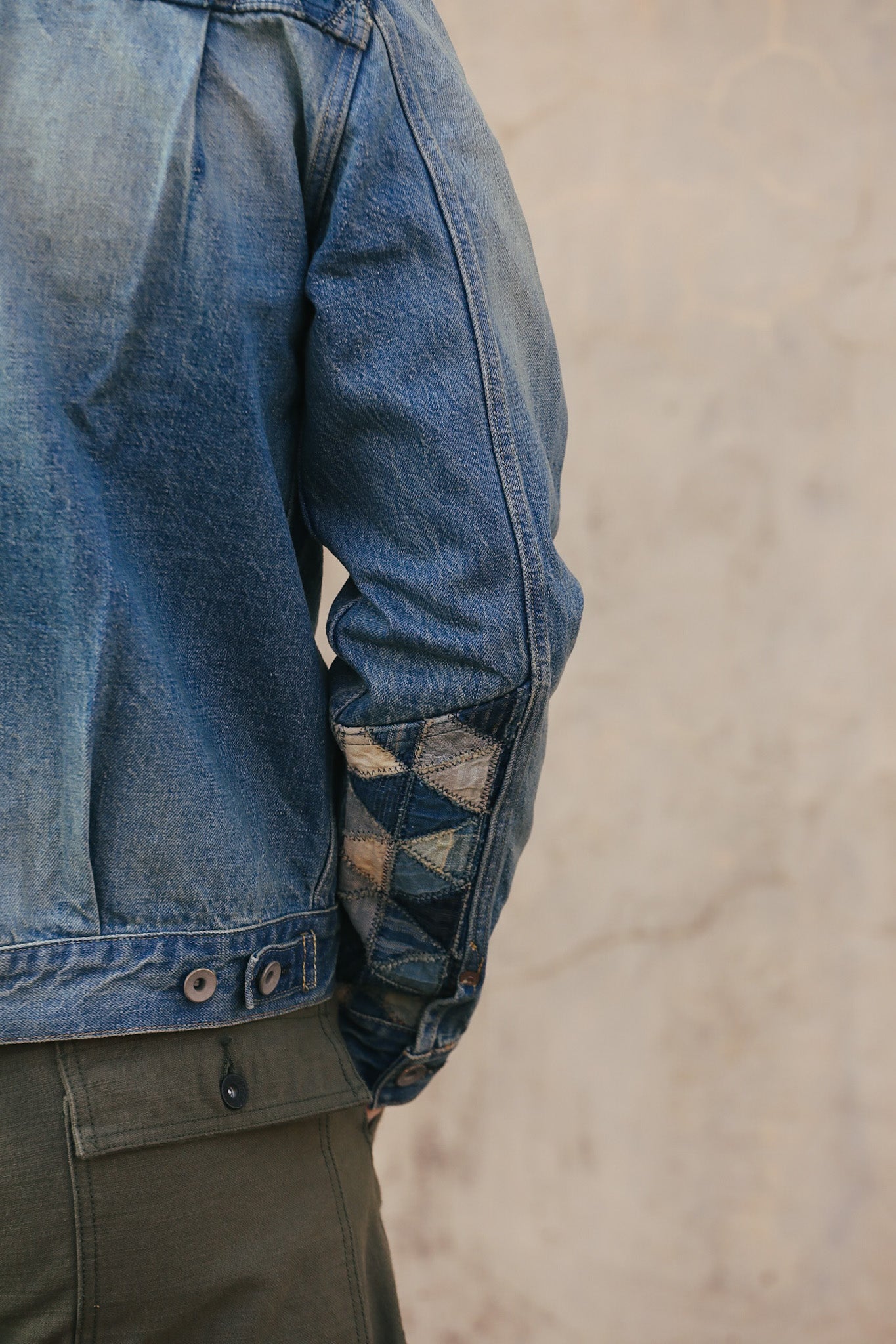 Close-up of a blue denim jacket with patchwork sleeve on a neutral background