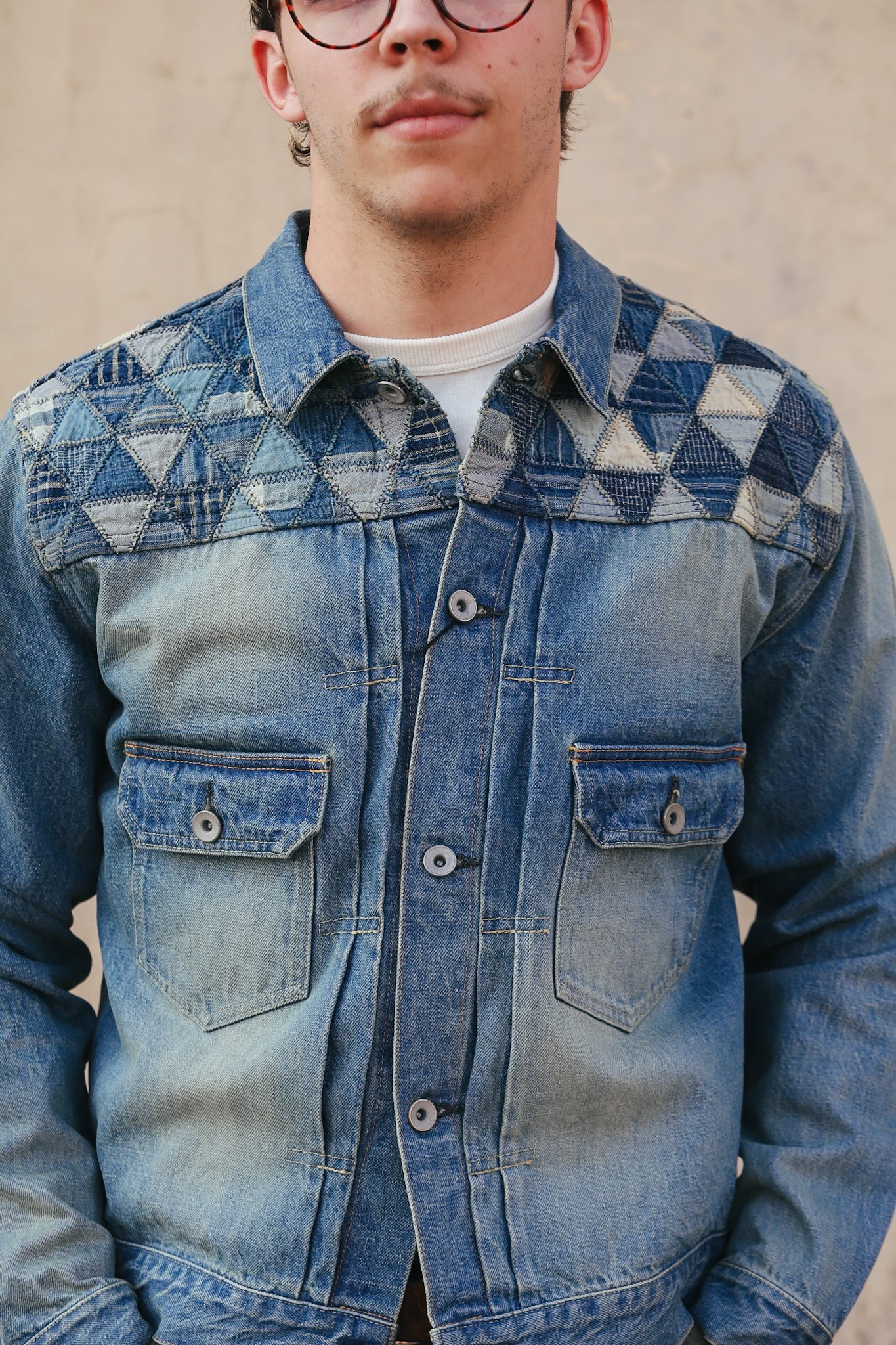 Person wearing a blue denim jacket with geometric pattern on a beige background