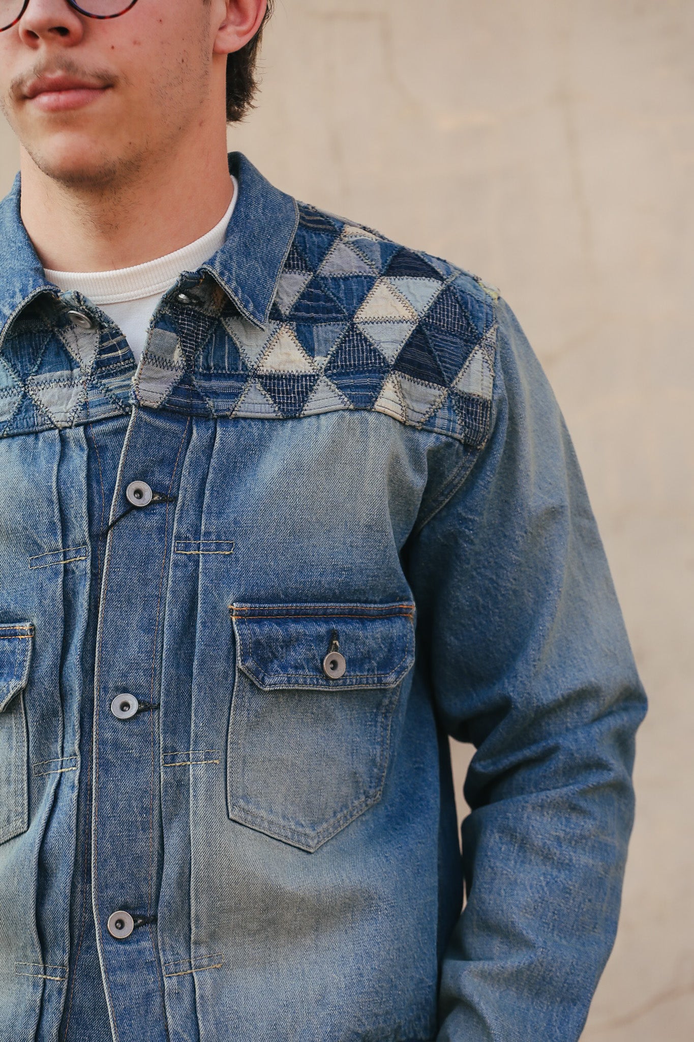 Person wearing a blue denim jacket with geometric pattern on a plain background