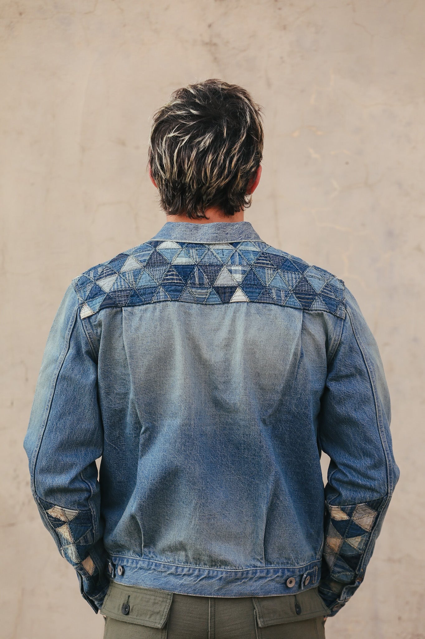 Person wearing a blue denim jacket with geometric patterns on a beige background
