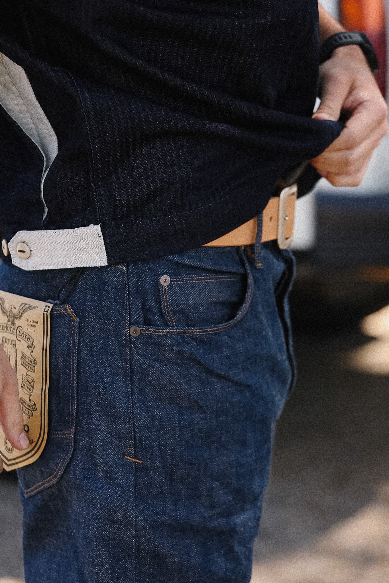 Person wearing blue jeans with a belt and a dark shirt, blurred background
