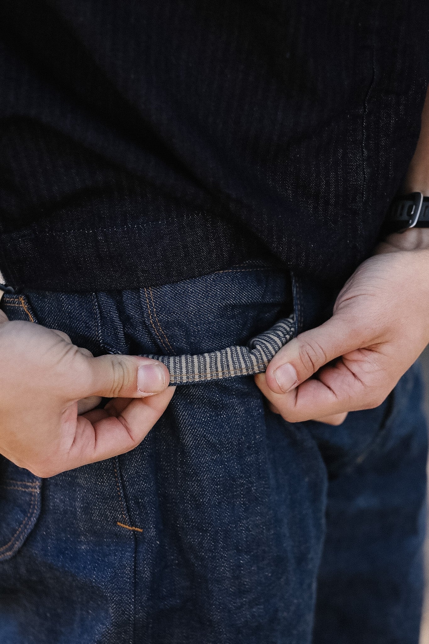 Person adjusting a belt on dark jeans with a blurred background