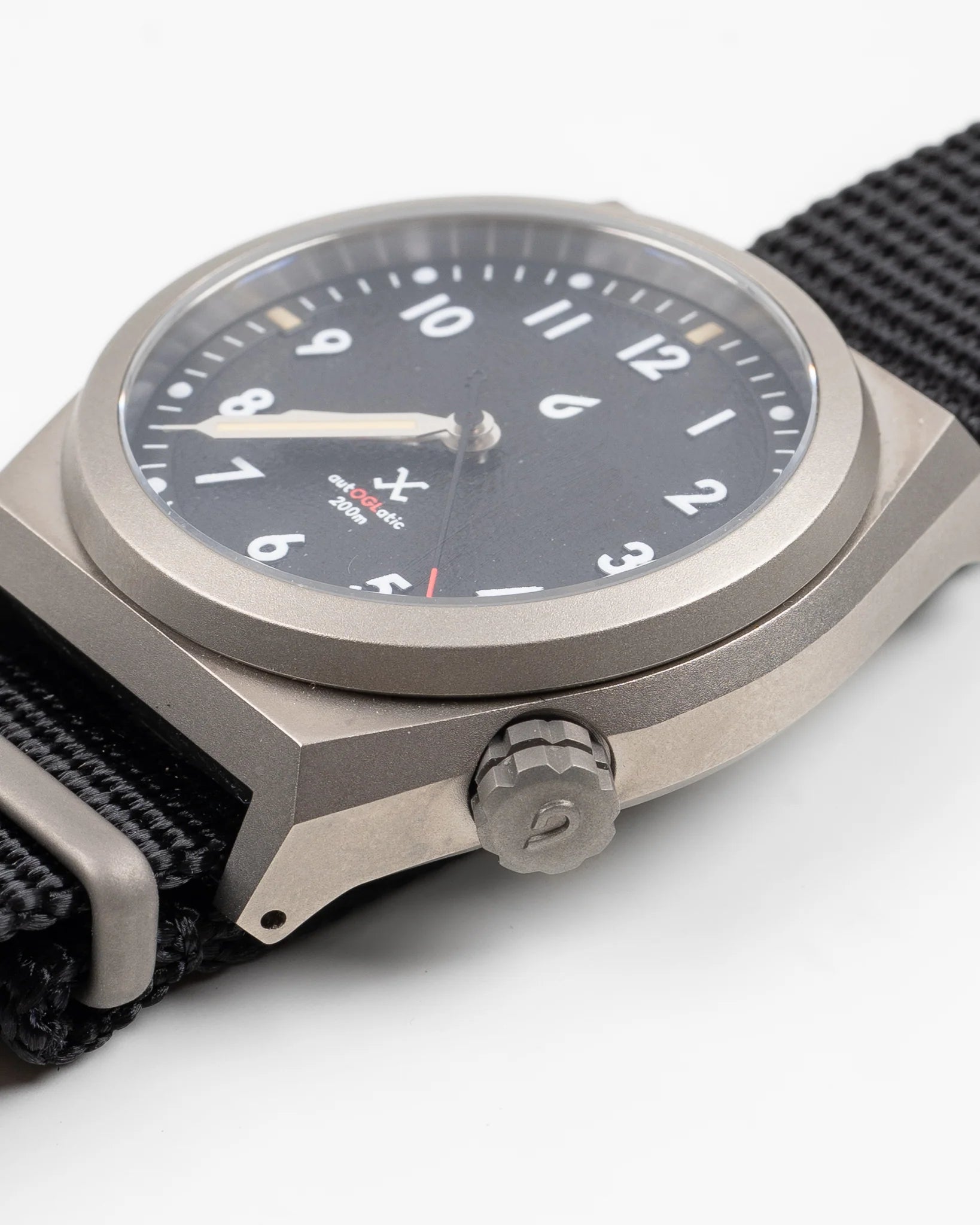Close-up of OGL autoGLatic bold MKI field watch with black dial and nylon strap on white background