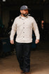Man wearing cream flannel Oxford shirt, dark jeans, and blue baseball cap in industrial workshop