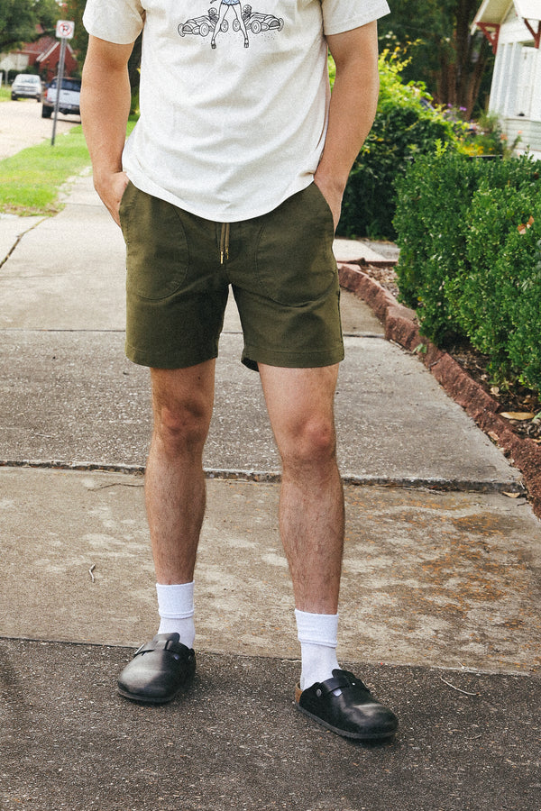 Man wearing olive green Premium Deck Shorts with white socks and black slip-on shoes on sidewalk