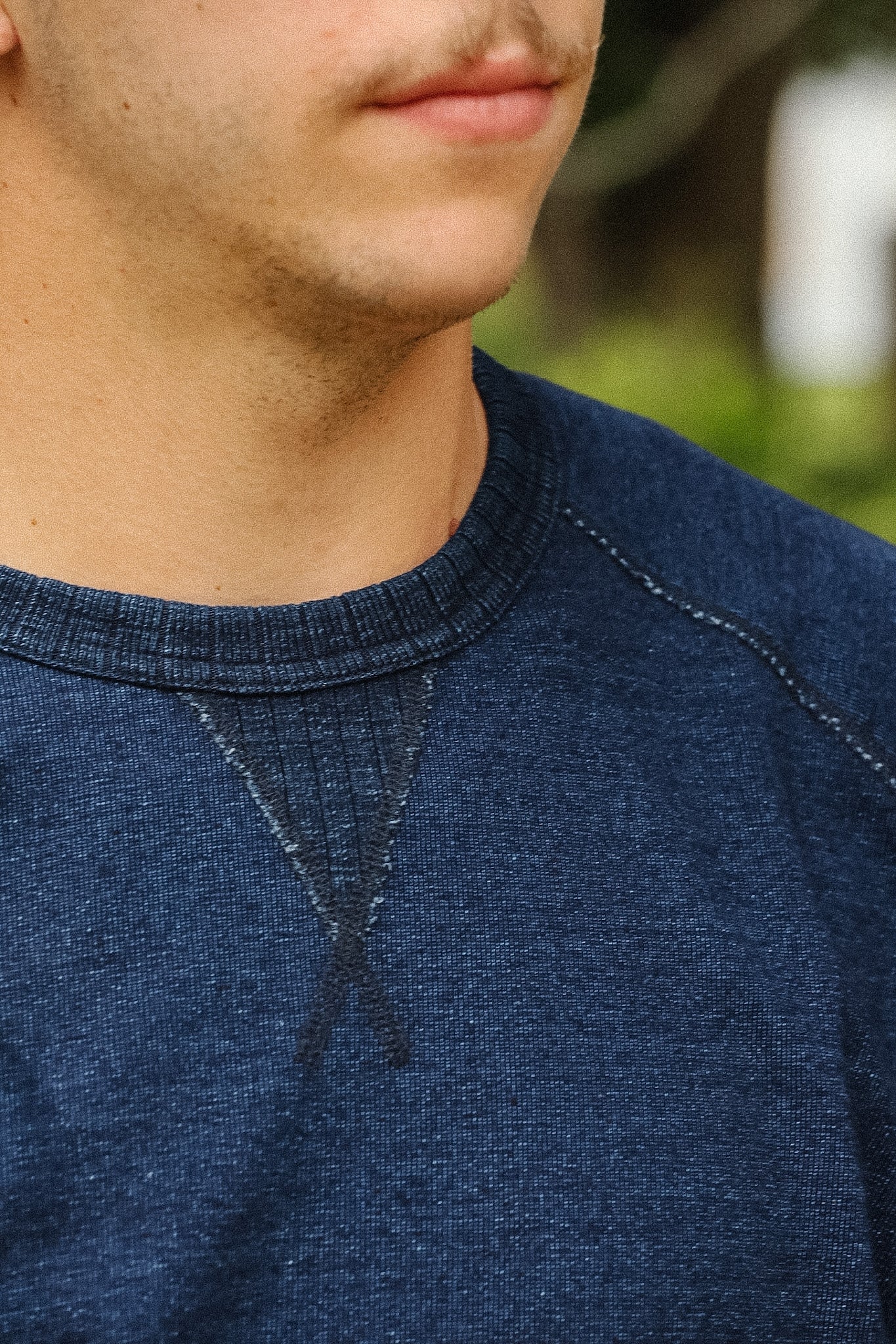 detail shot of a textured blue shirt with a green foliage background. 