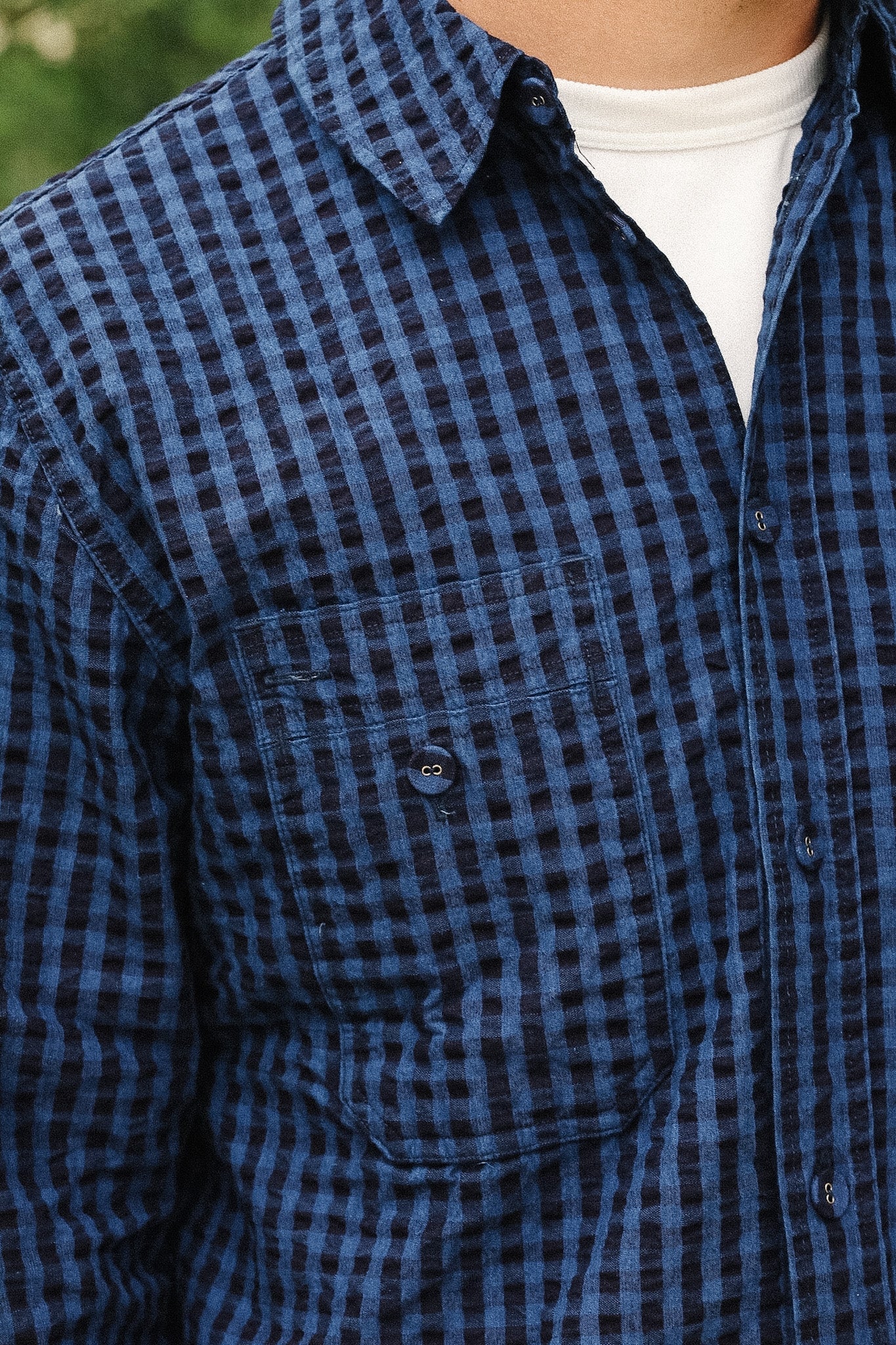 Close-up of a person wearing a blue and black checkered button-up shirt over a white undershirt.