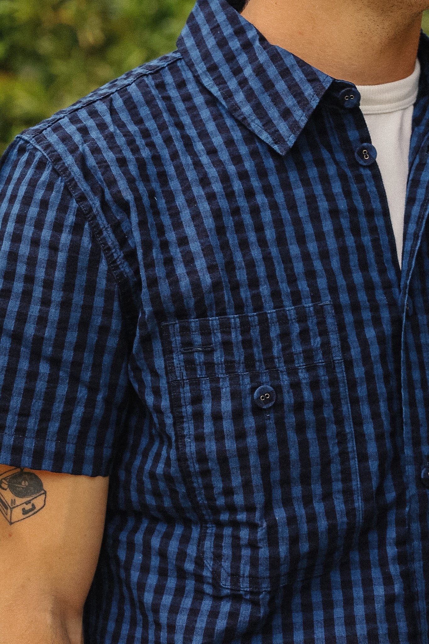Close-up of a man wearing a short-sleeve button-up shirt with a blue and black gingham check pattern, layered over a white t-shirt.