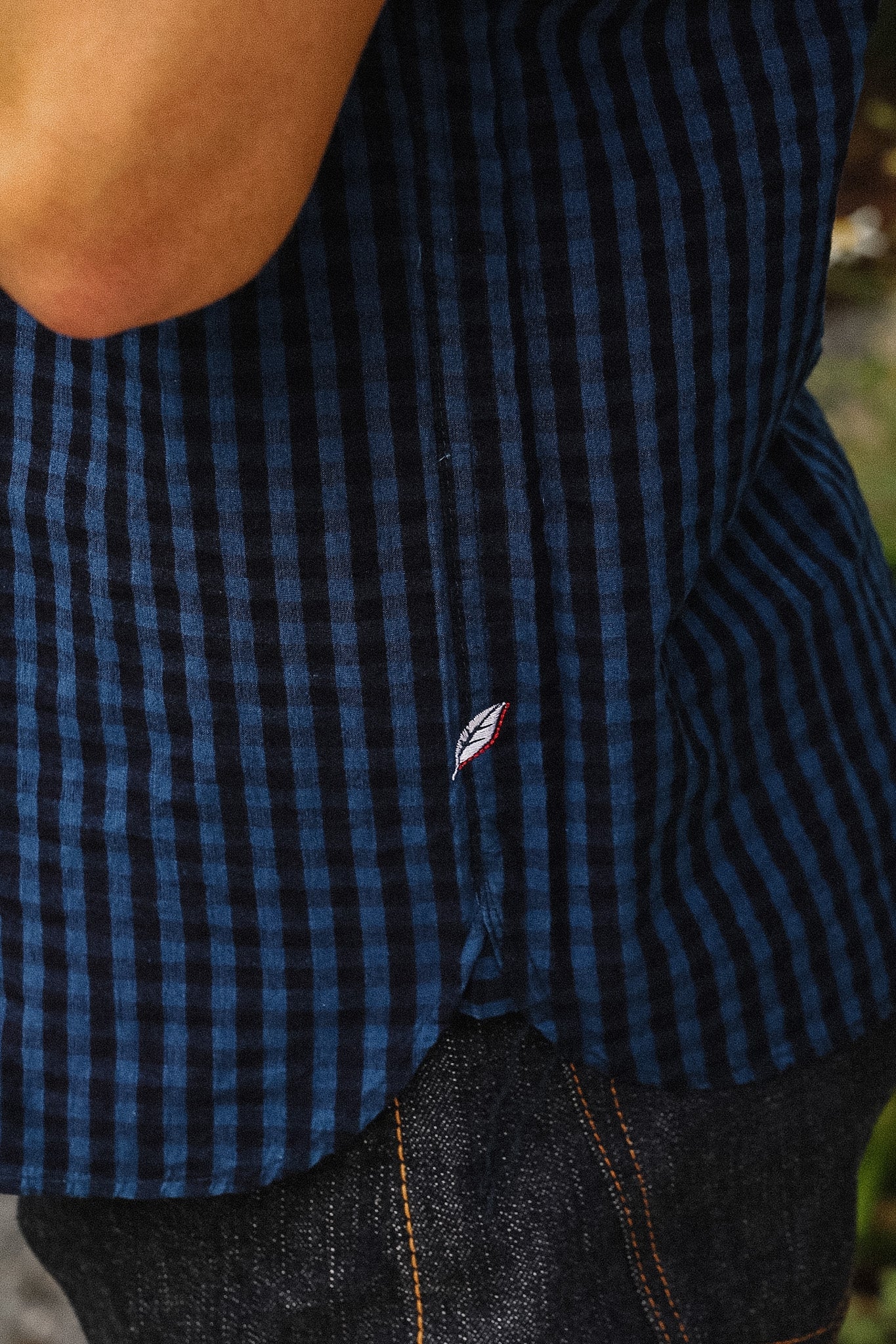 Close-up of a person wearing a short-sleeve button-up shirt with a blue and black gingham check pattern, layered over a white undershirt.