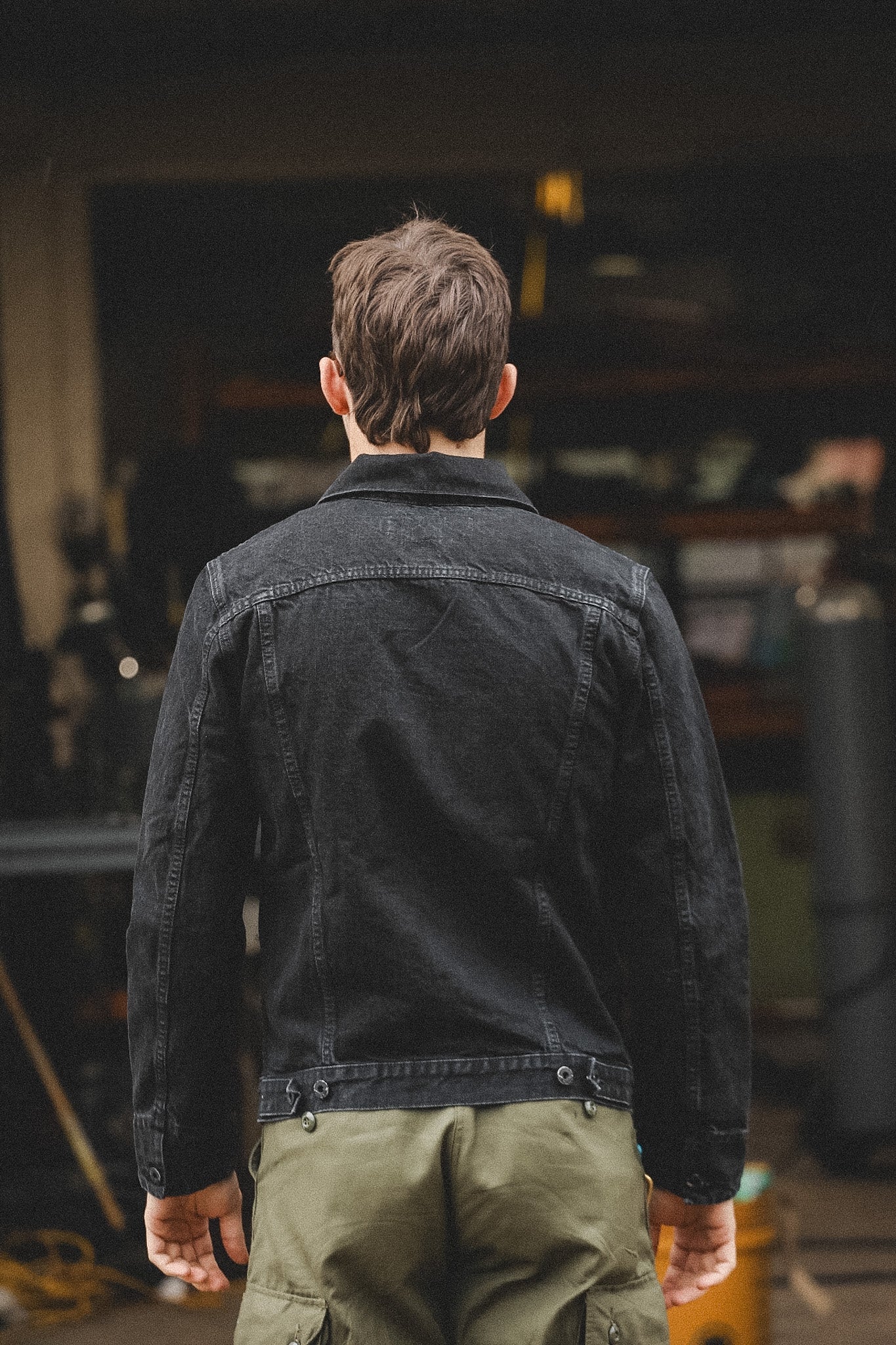 Person wearing a black jacket and green pants standing in a garage.