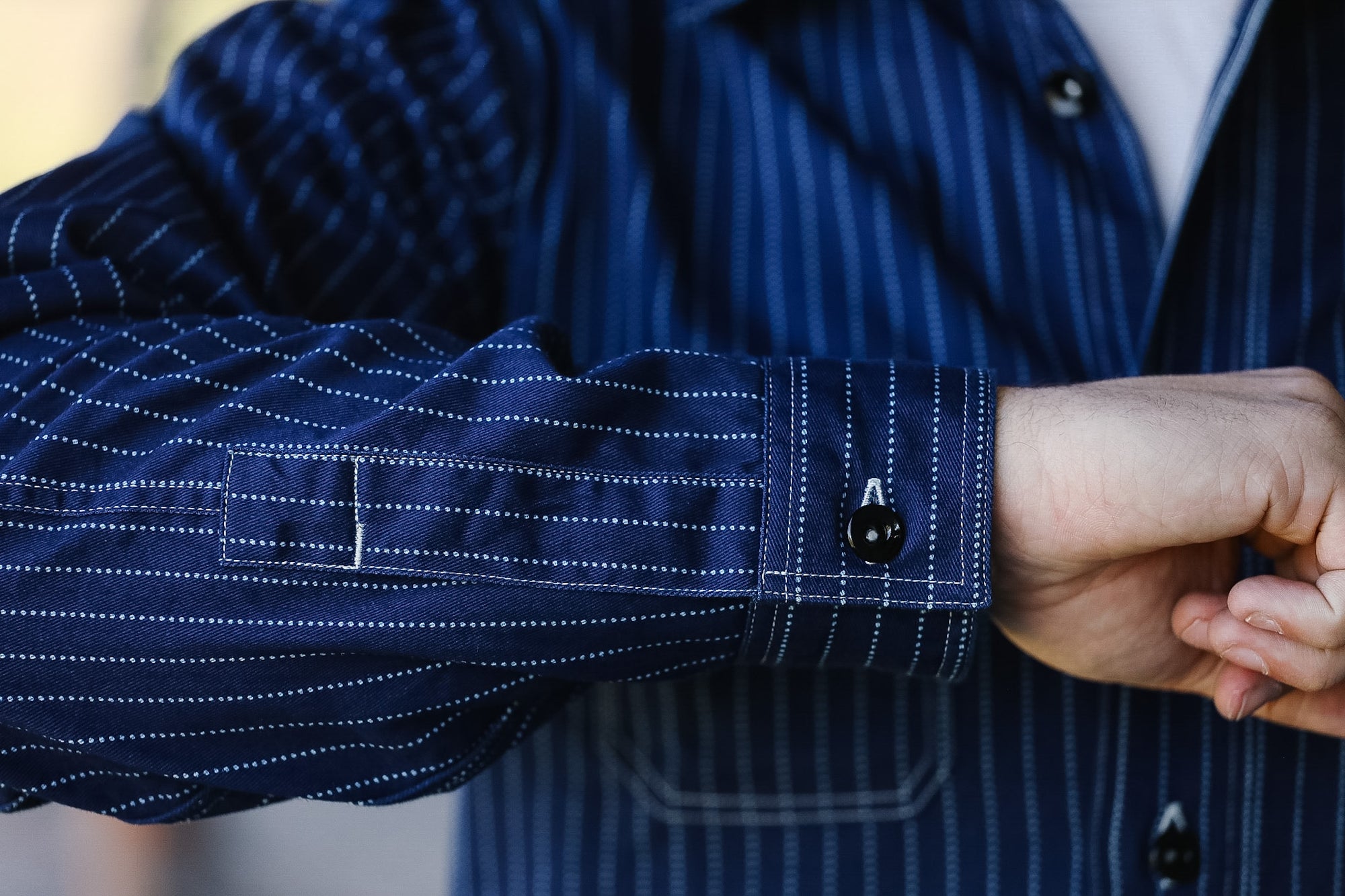 Close-up of a person wearing a blue pinstripe shirt with rolled-up sleeves.