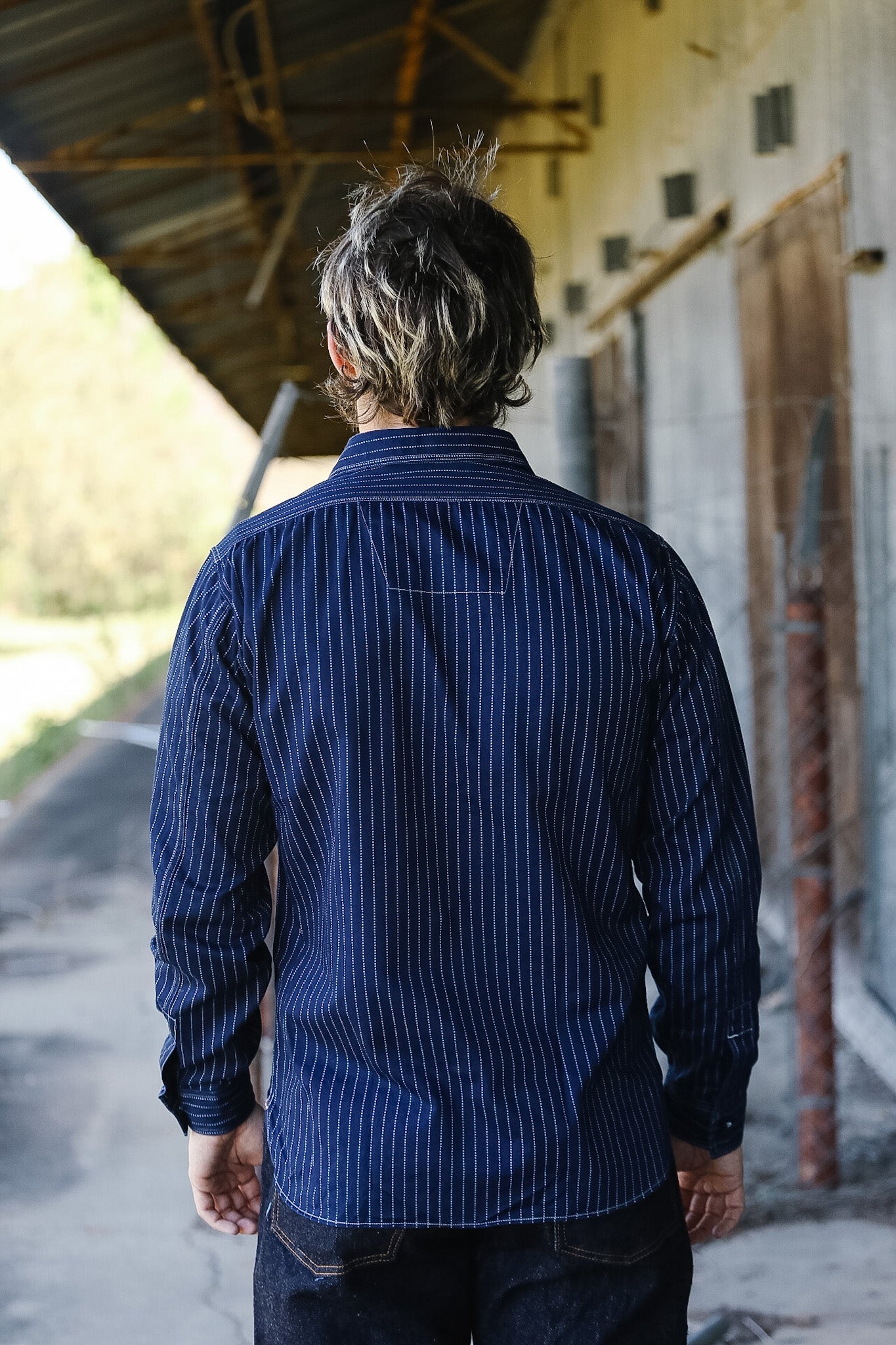 Person wearing a blue striped shirt standing under a sheltered area.