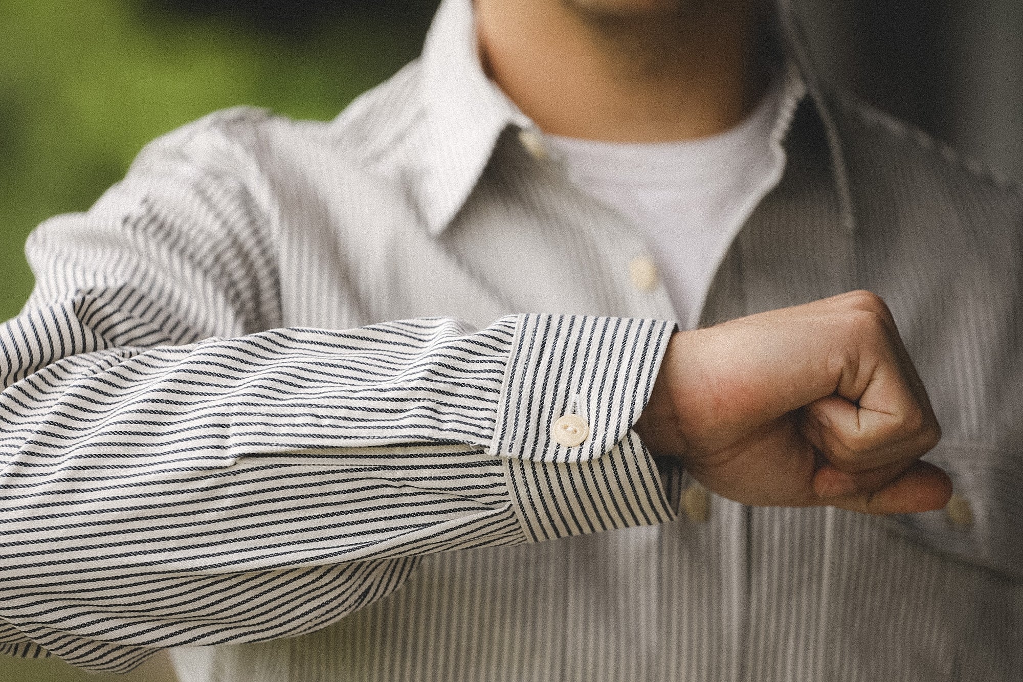 Person wearing a striped shirt with rolled-up sleeve, blurred background