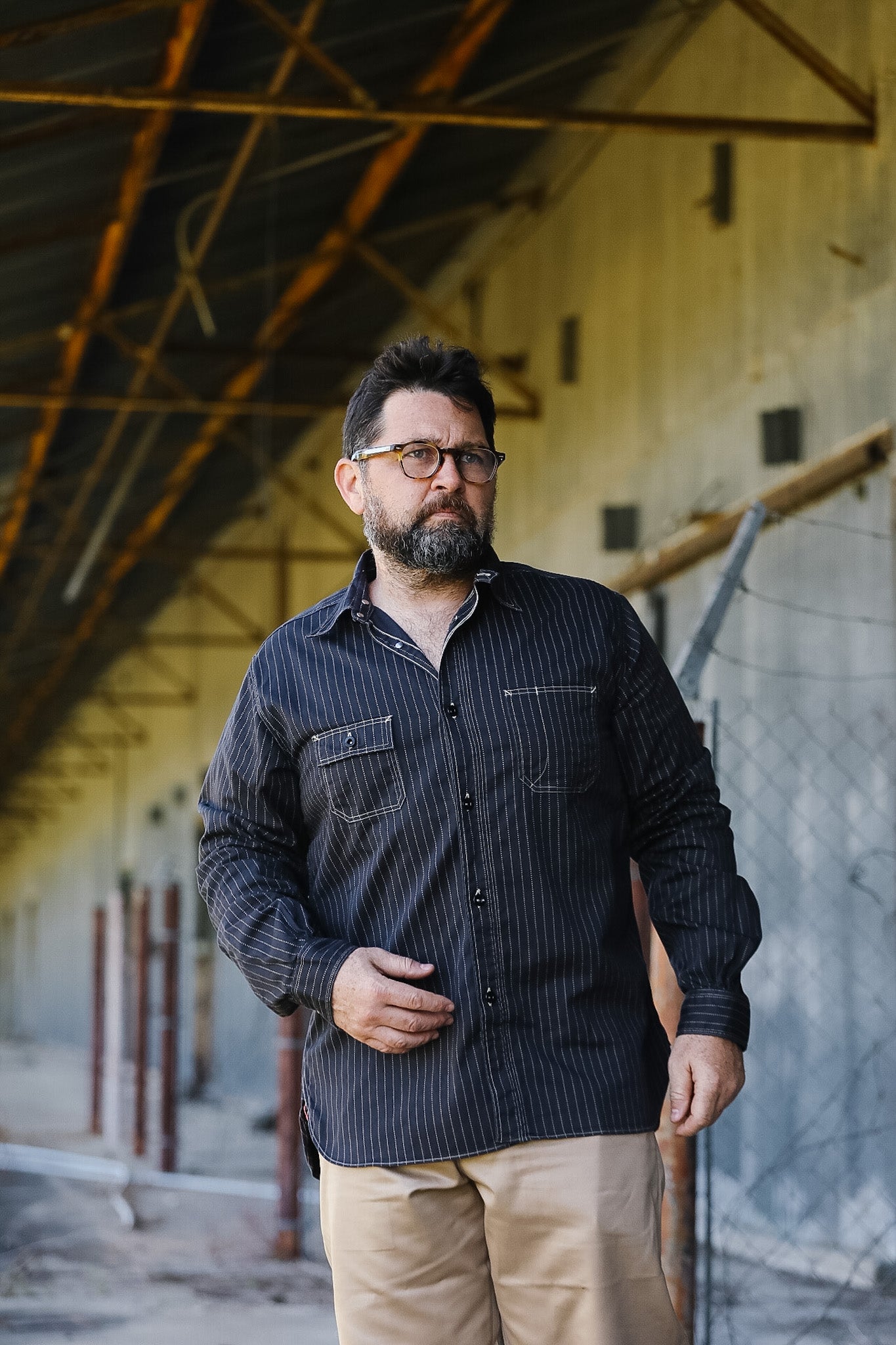 Man wearing a dark shirt and beige pants standing in an industrial setting