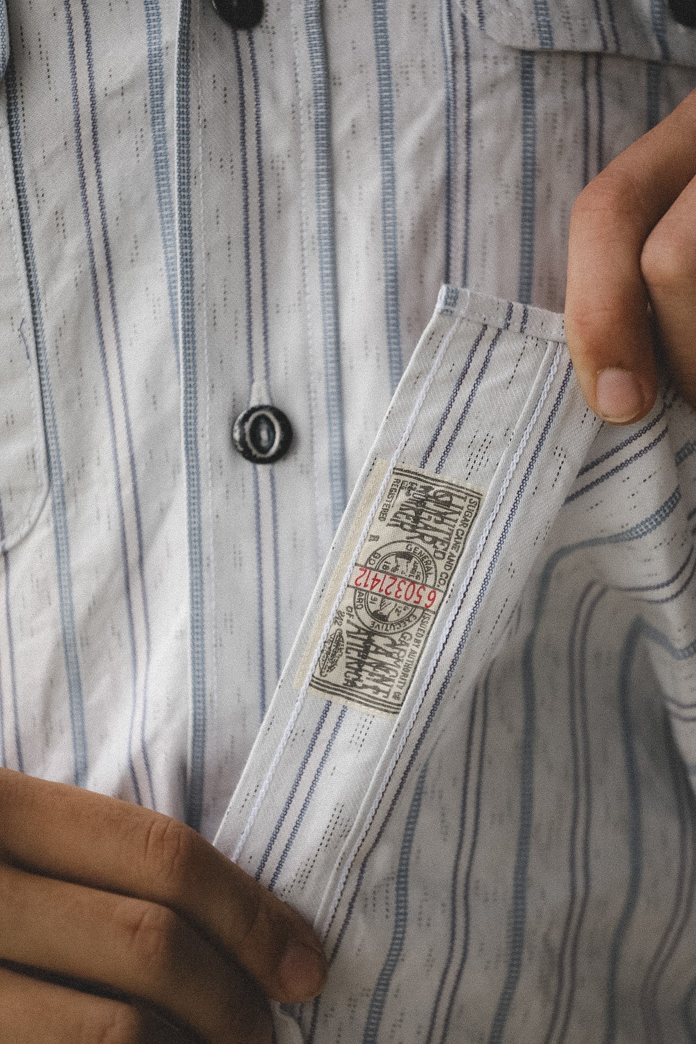 Person holding a small paper label with text and graphics on a striped shirt background