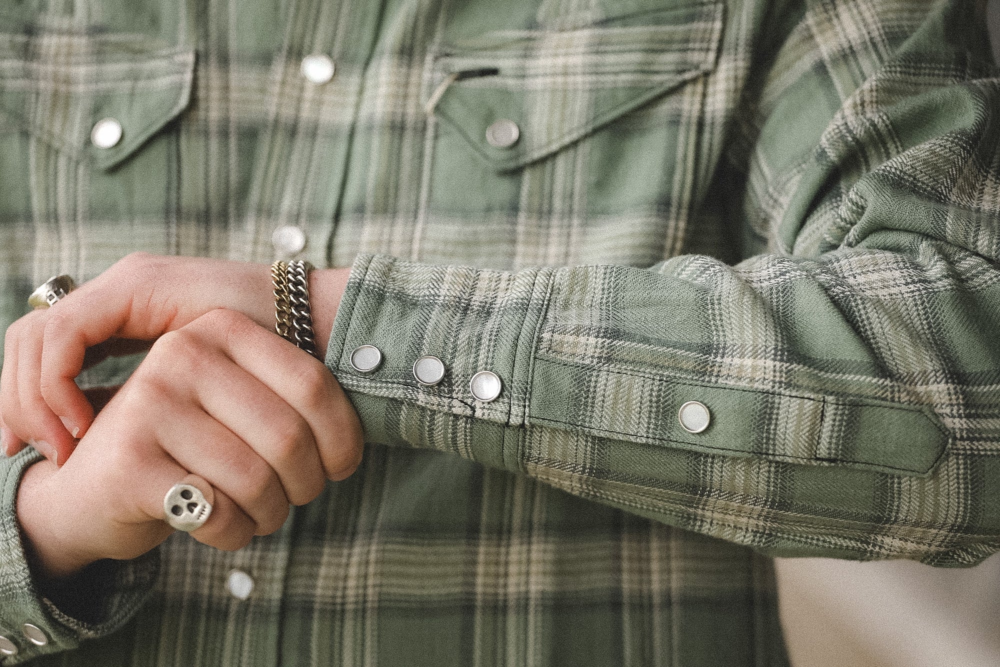 Close-up of a person wearing a green plaid shirt with buttons and jewelry.
