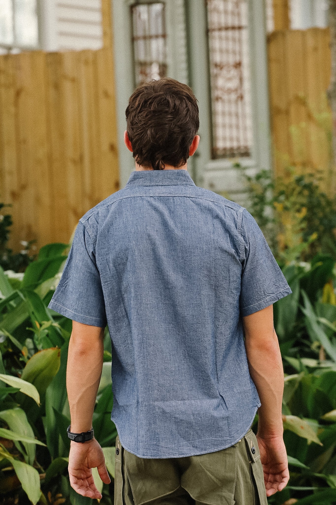 Person wearing a blue shirt standing in a garden with plants and a wooden fence in the background