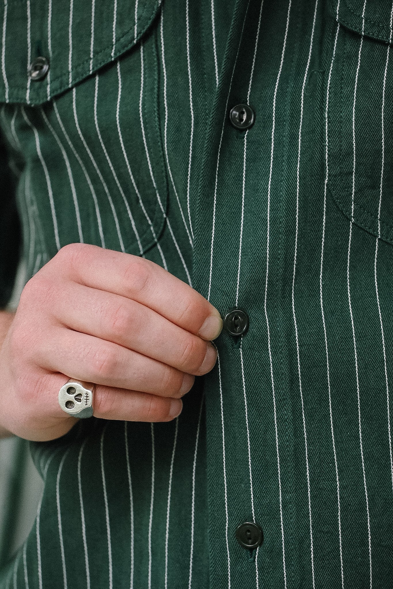 Close-up of a person wearing a green pinstripe shirt with a hand buttoning it.