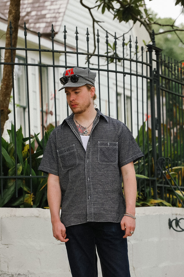 Man wearing a checkered shirt and cap standing in front of a black metal fence.