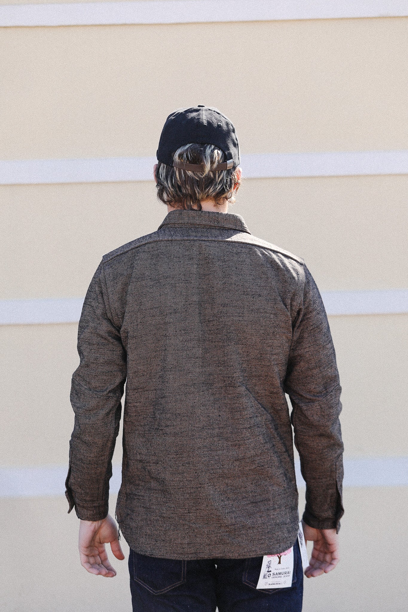 Person wearing a brown jacket with a visible brand label against a beige wall.