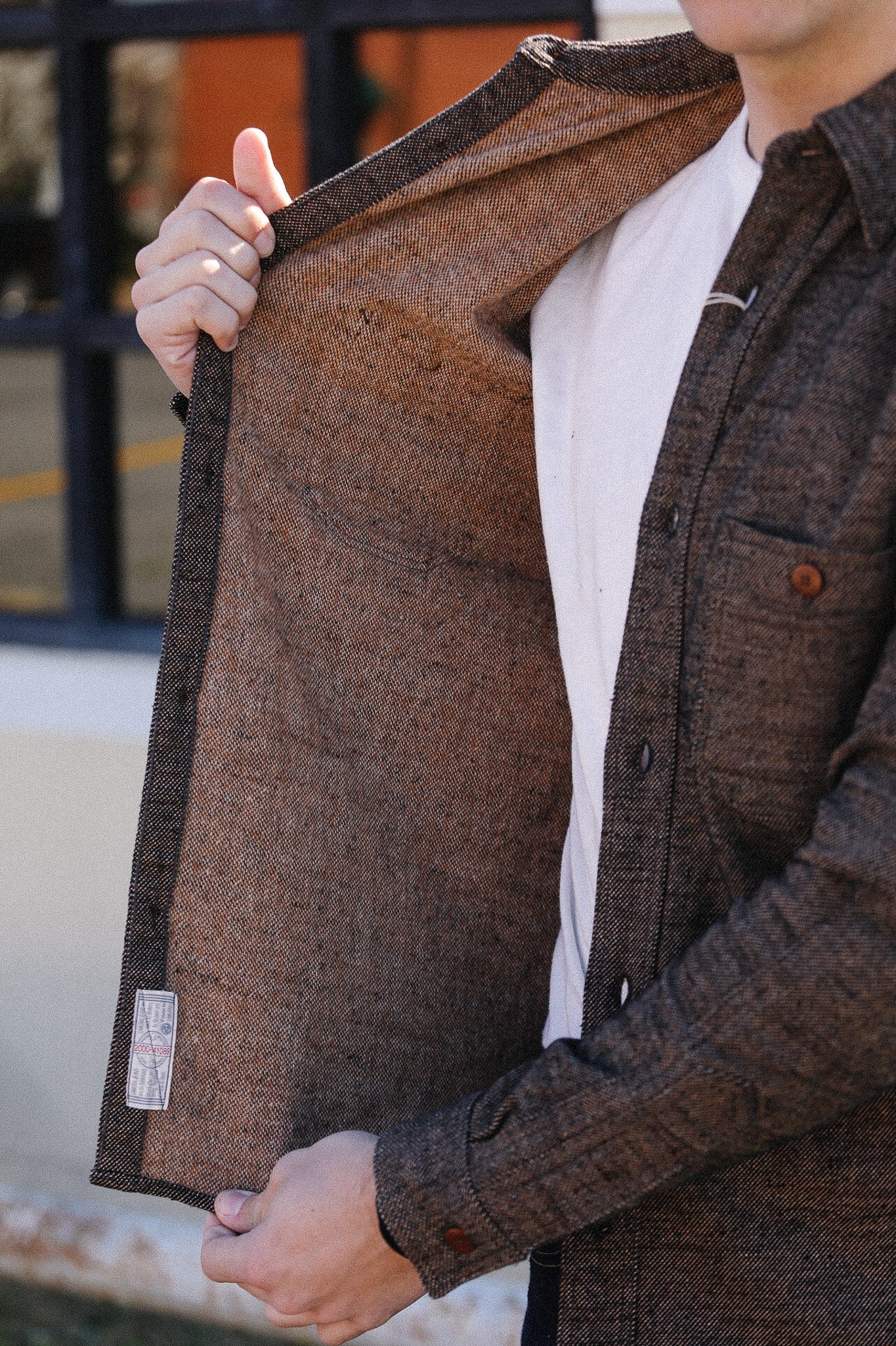 Person holding a brown textured jacket outdoors