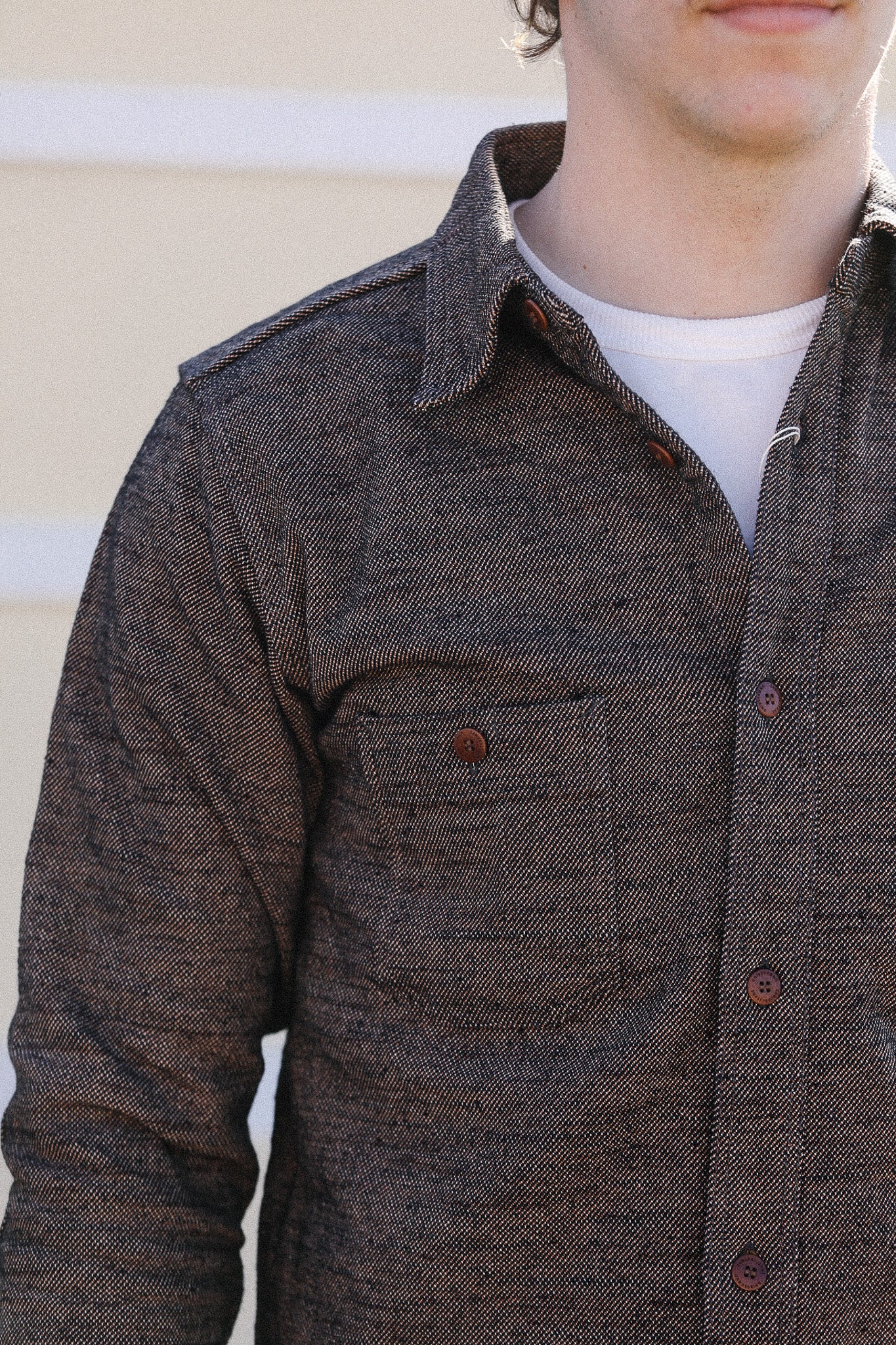 Close-up of a person wearing a brown button-up shirt with a neutral background