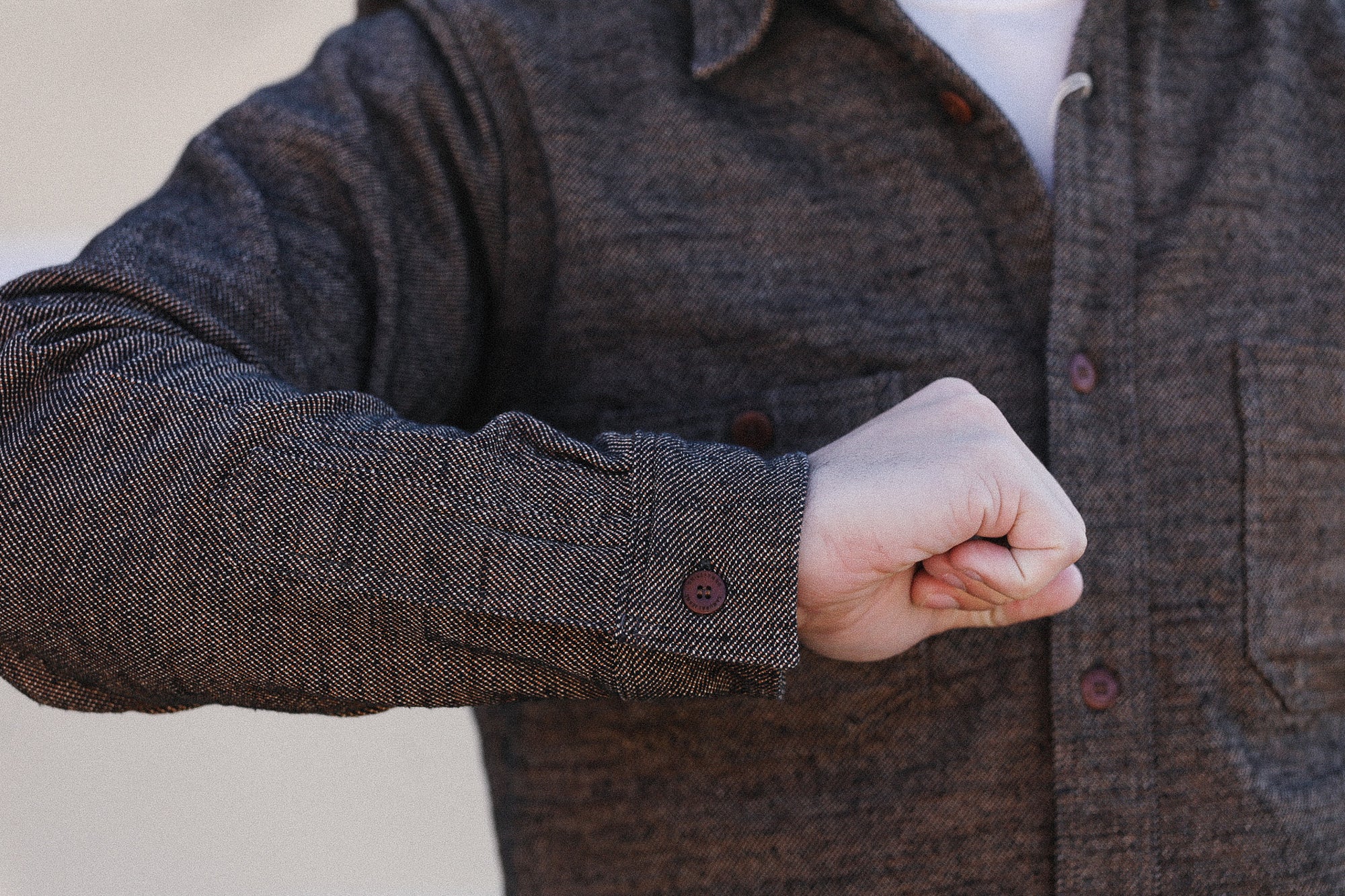 Person wearing a brown button-up shirt with a blurred background